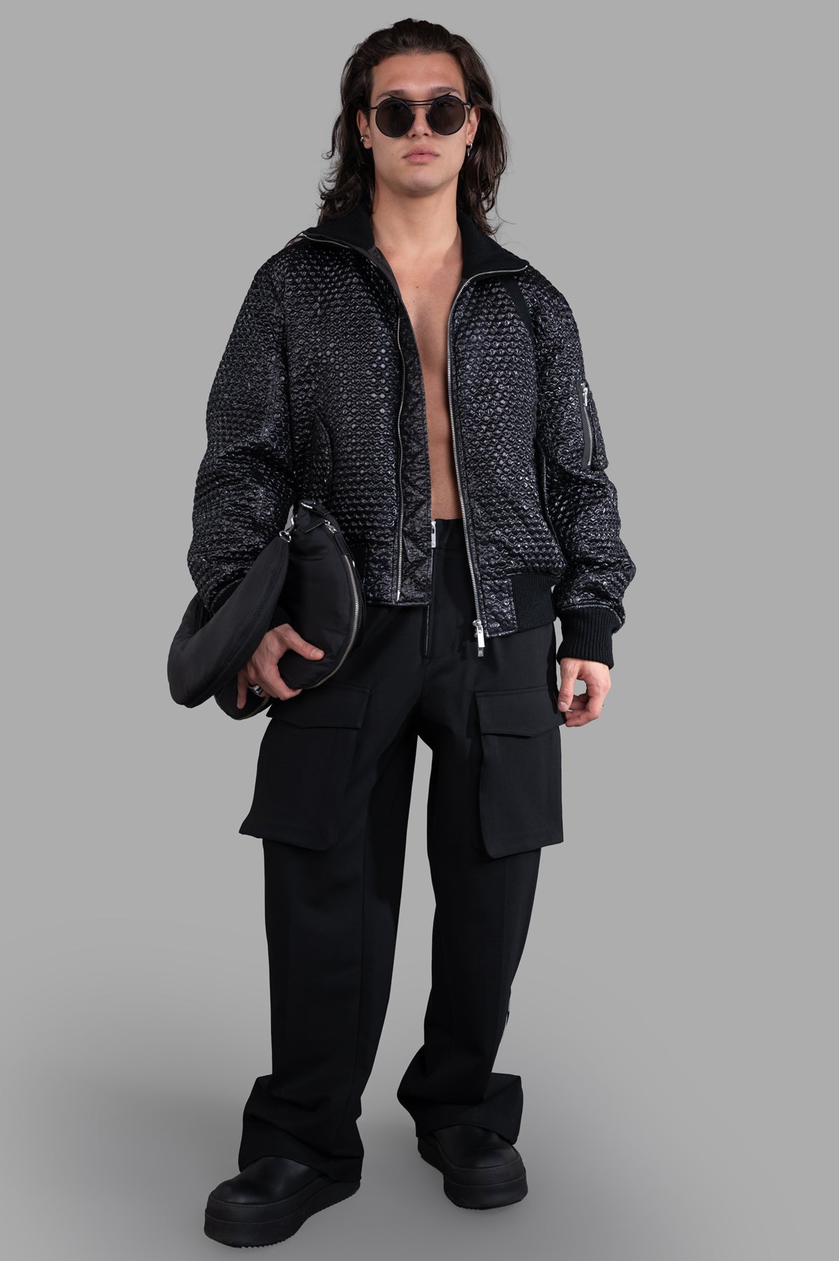 Helmut Lang Seatbelt Bomber in black, worn by model. Features 3D bubblewrap texture, ribbed collar, and cuffs. Unisex fit.
