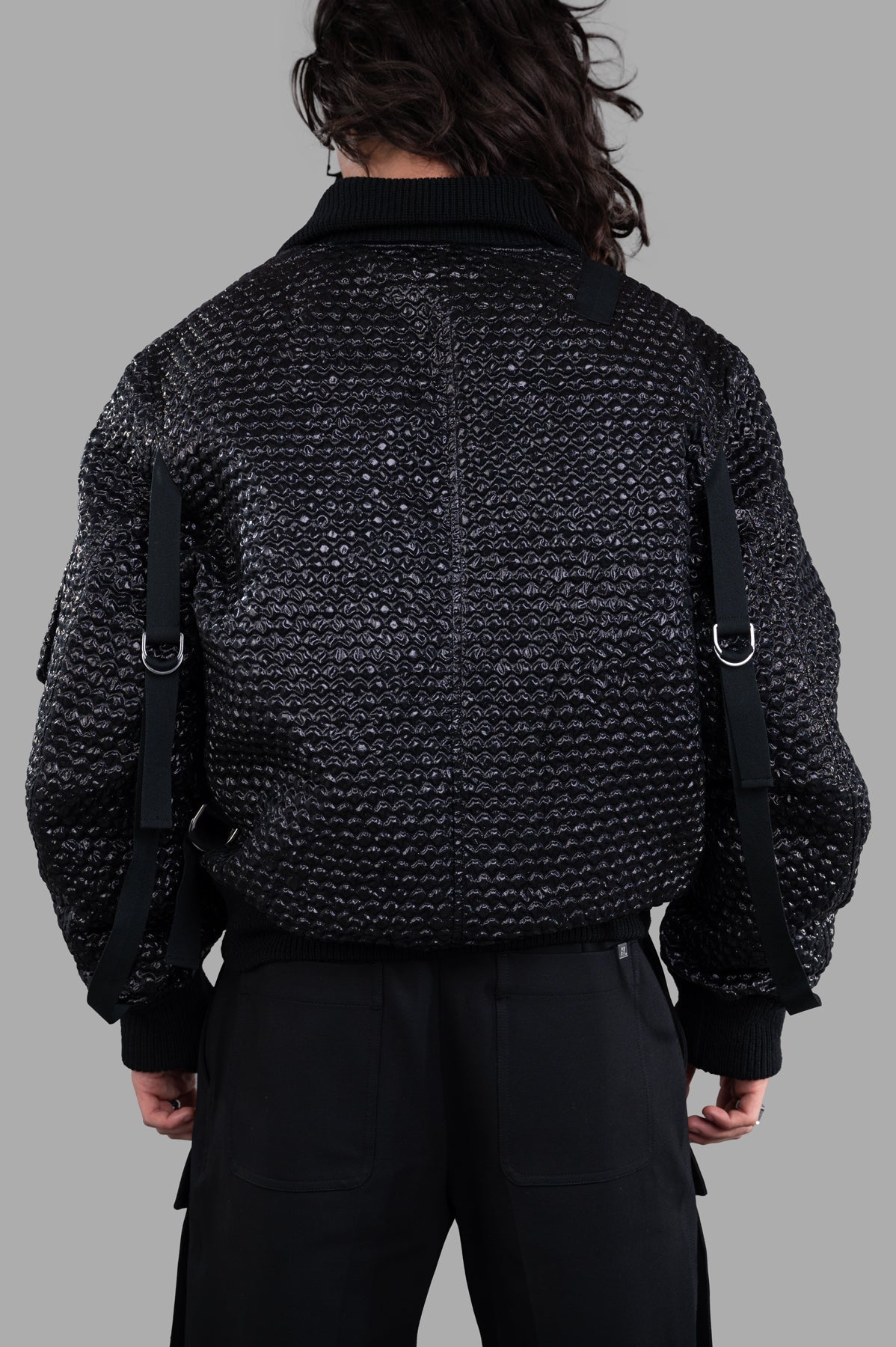 Helmut Lang Seatbelt Bomber jacket showcasing a textured black jacquard design with utility straps from the back view.