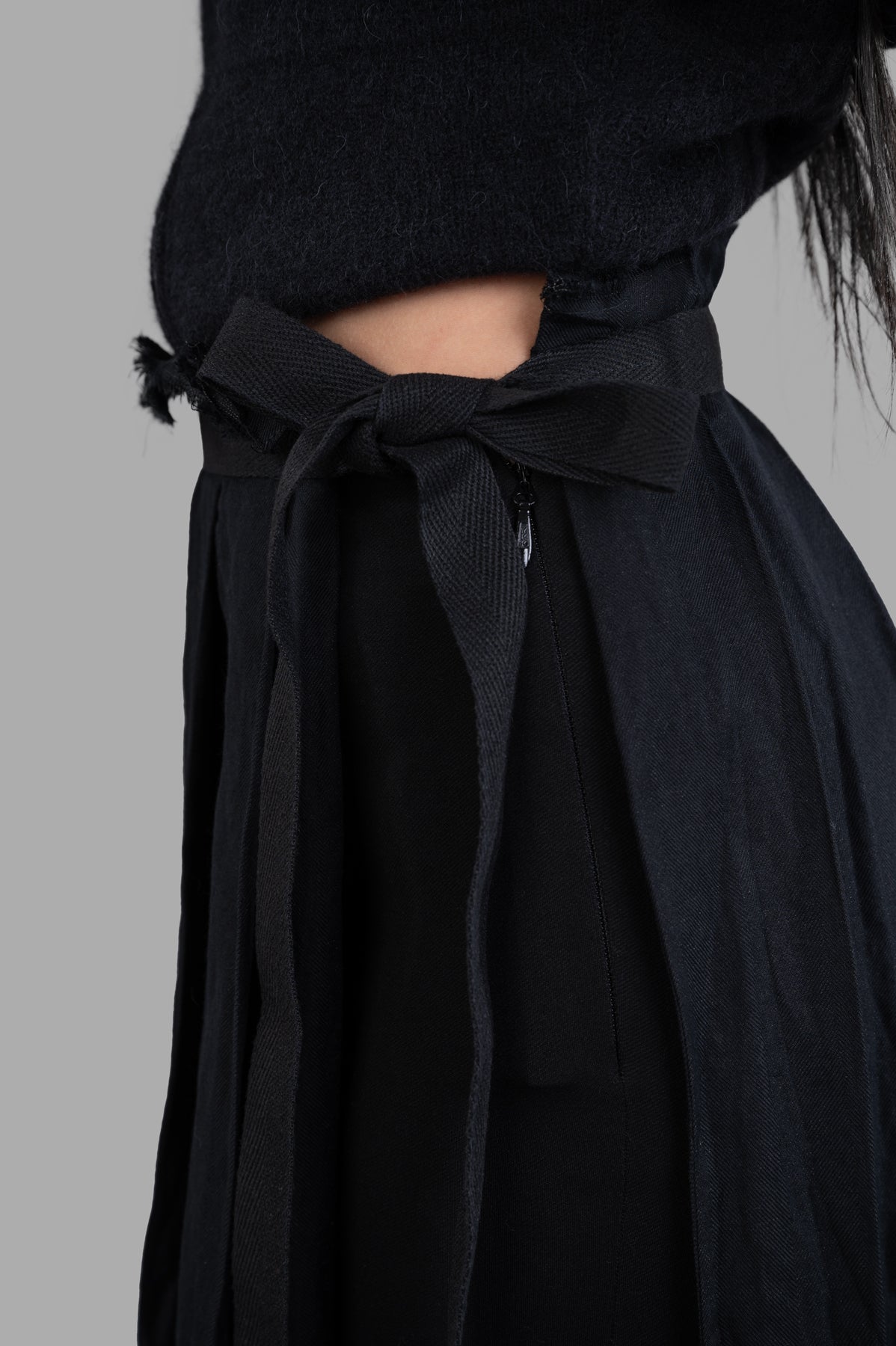 Masnada Pleated Maxi Skirt close-up of the tied waistband and zipper detail, showcasing fabric texture in black.
