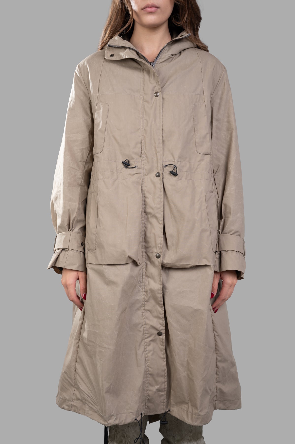 Masnada Layered Raincoat in beige, featuring a ripstop texture, drawstring hood, and belted cuffs. Shown on model.