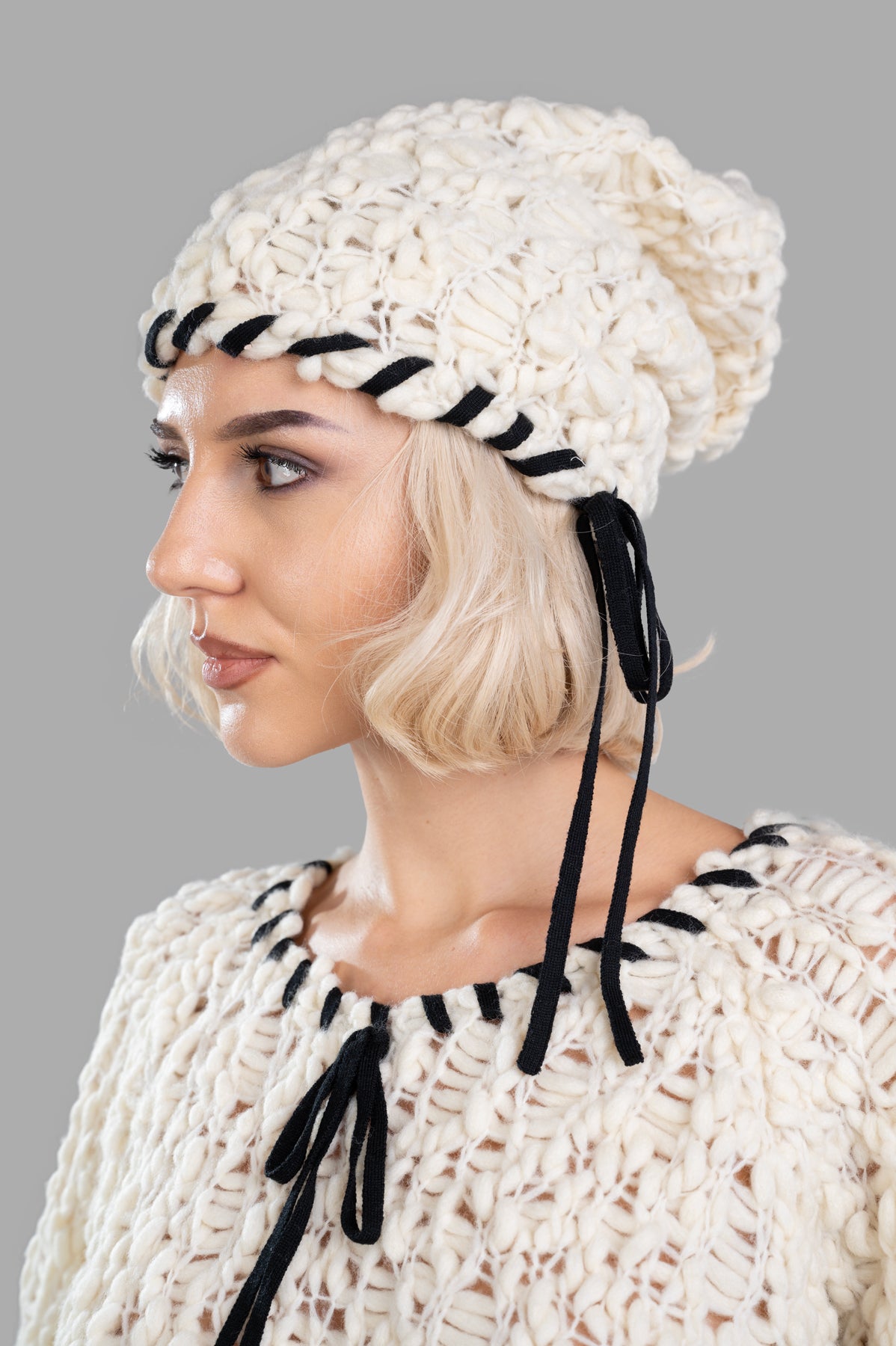 By Malene Birger Mossy Wool Hat shown on model, featuring a textured white knit and contrasting black tie-string details.