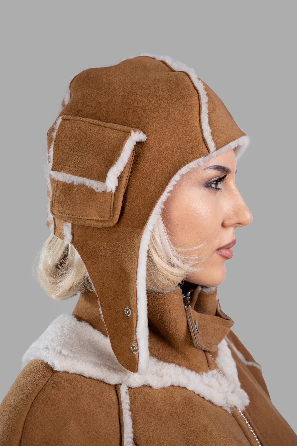 Natasha Zinko Shearling Camping Hat in brown, featuring an aviator design and faux fur lining, shown on a model's side.