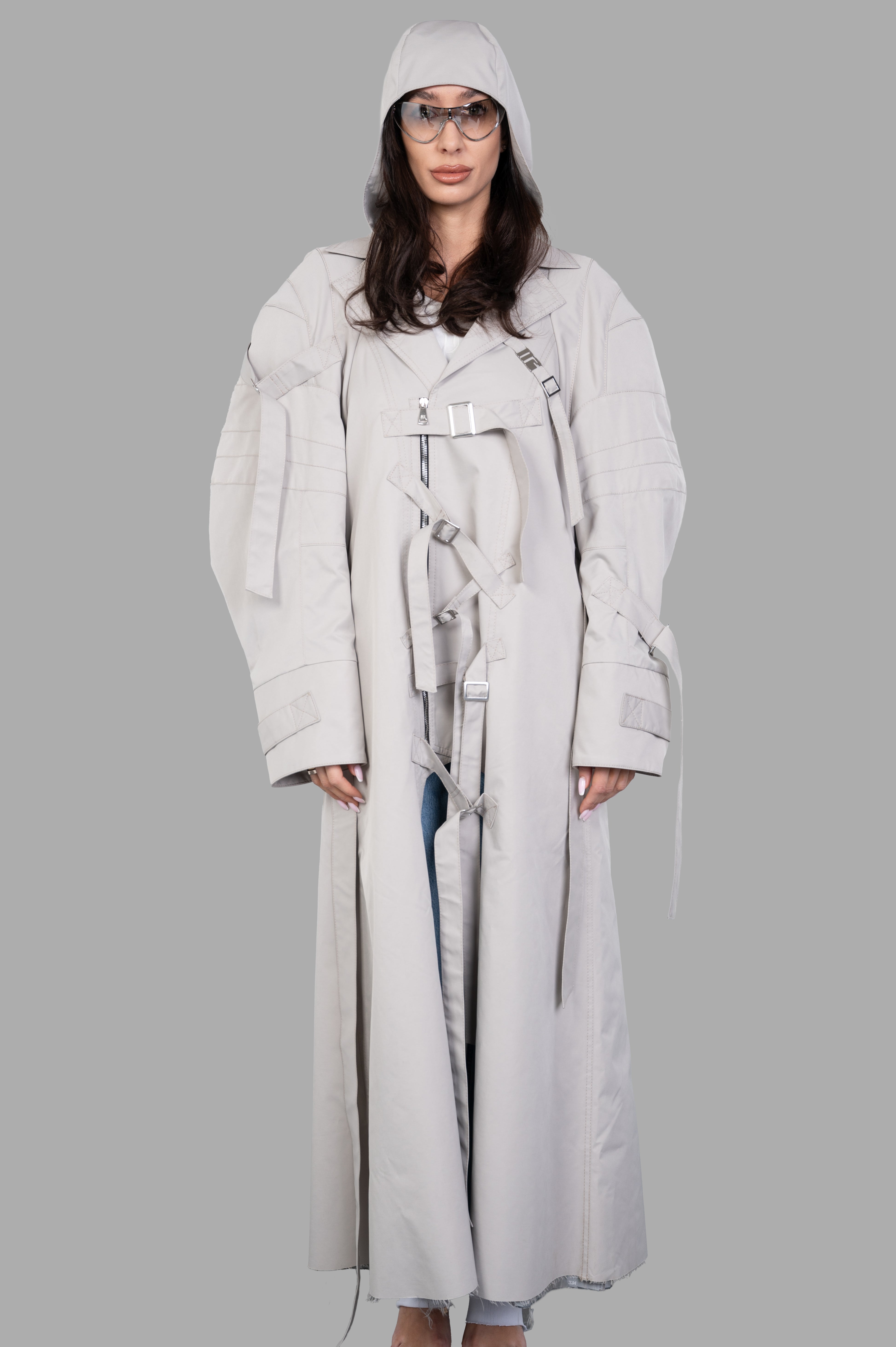 Natasha Zinko Strapped Trench on model, featuring hood, double-breasted zip, sleeve straps, and oversized fit in light gray.
