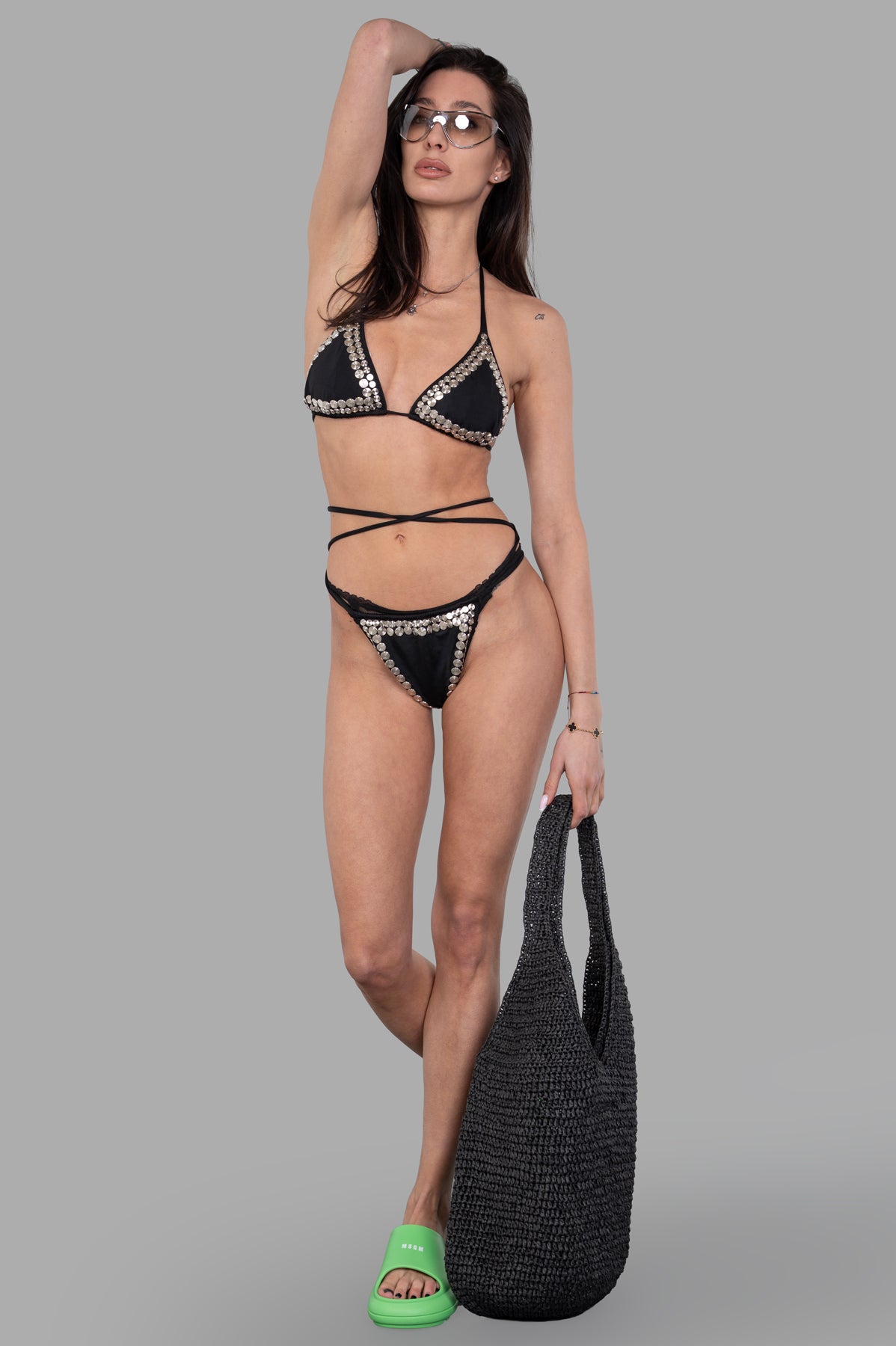 Norma Kamali Stud Criss-cross Bikini front view, black triangle top, criss-cross straps, high-cut leg, on-model with bag.
