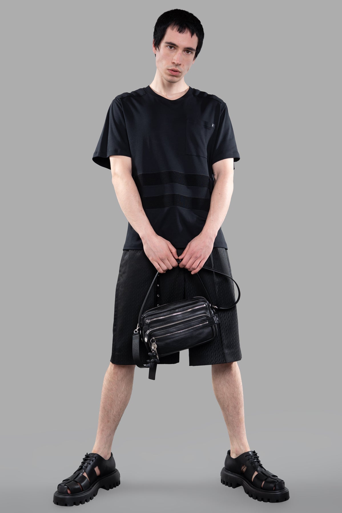 Helmut Lang Armor T-shirt shown on-model front view with black shorts and matching sandals, holding a black bag.