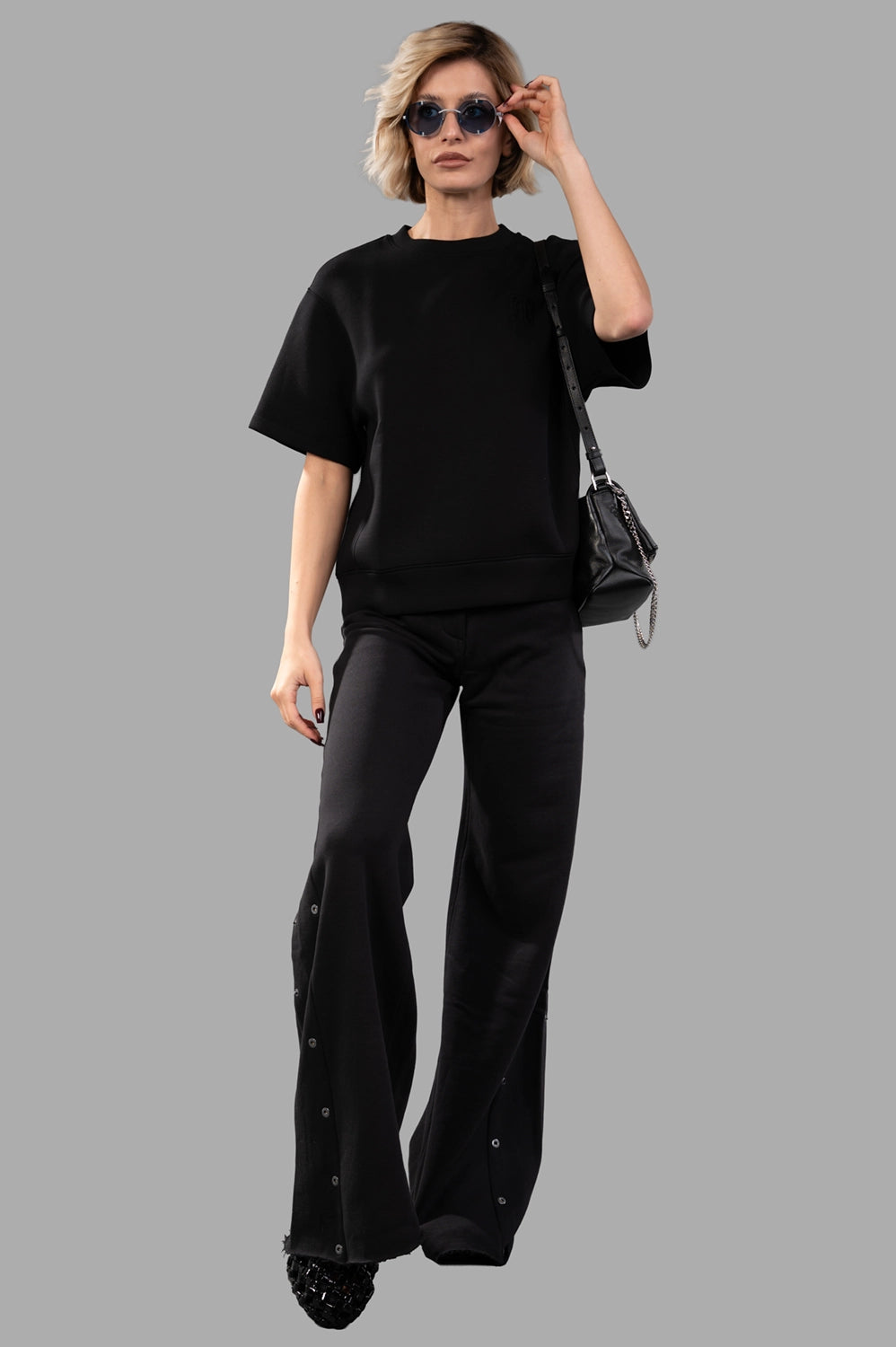 Full-length view wearing black short-sleeve sweatshirt with crew neck, dropped shoulders and tonal monogram, styled with black pants