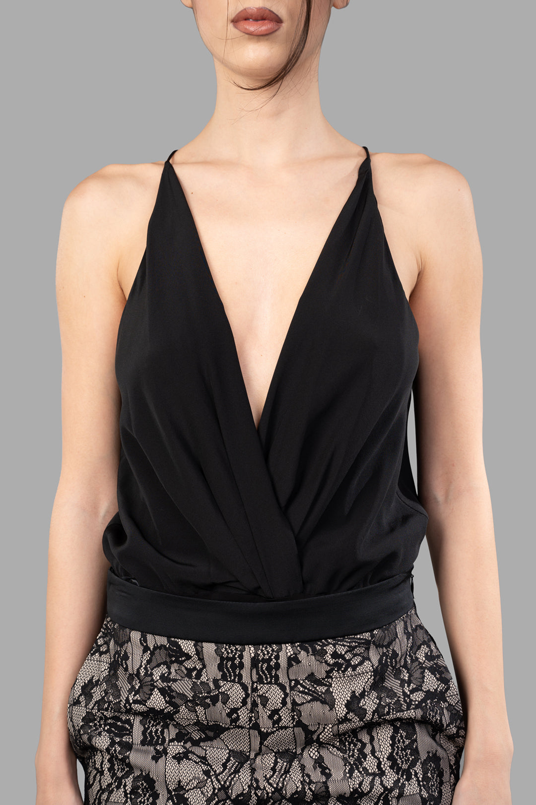 Anine Bing Shiloh Bodysuit featuring a deep V-neckline and draped front, showcased on a model against a gray backdrop.