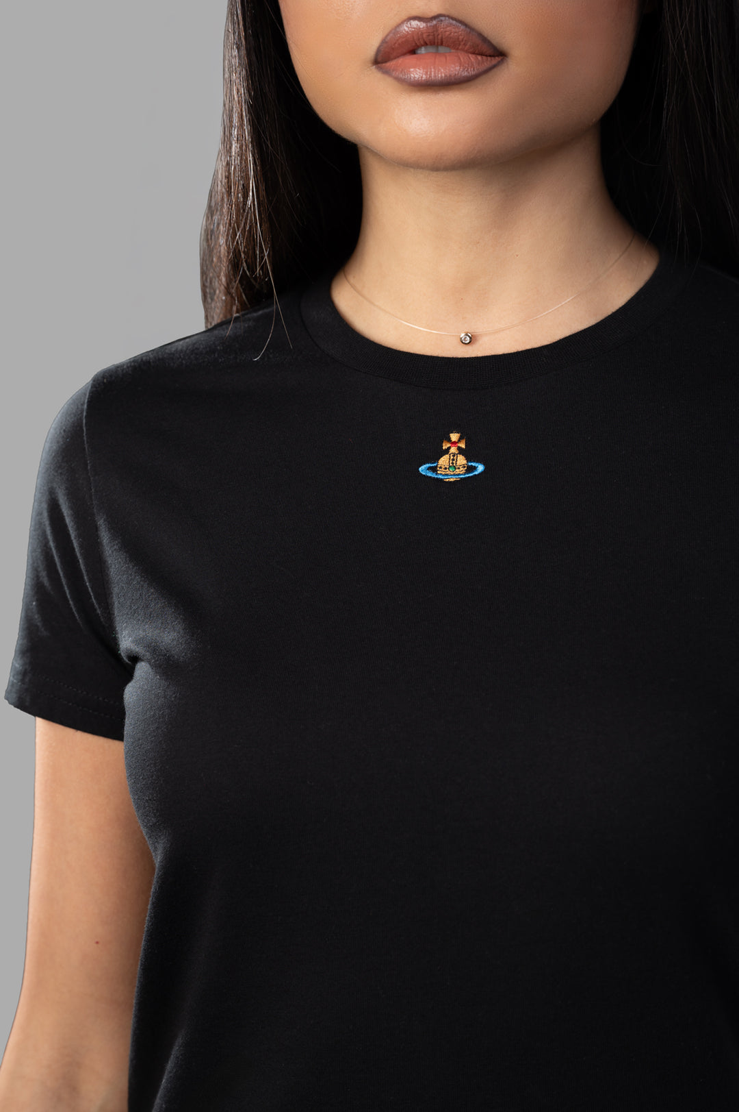 Vivienne Westwood. Close-up of the Orb Logo T-shirt featuring an embroidered orb on a model wearing a black crewneck top.