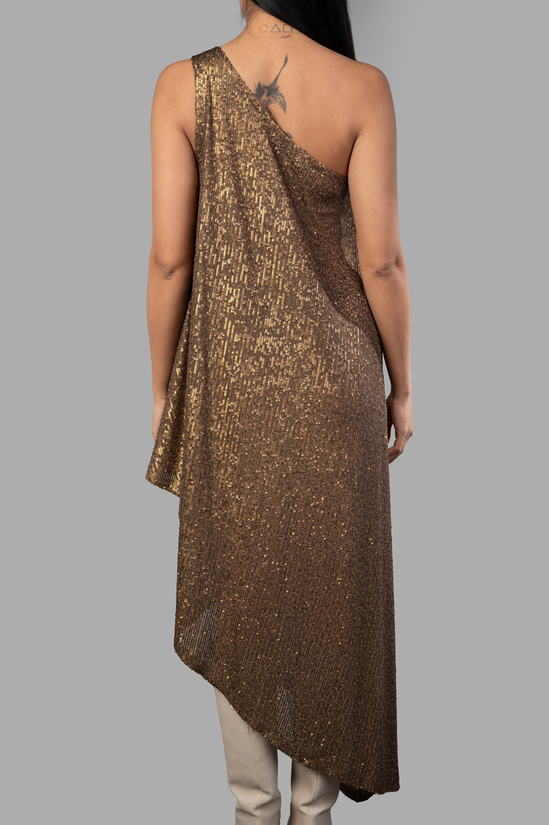 Norma Kamali One-shoulder Diagonal Tunic in bronze, showcasing a sequin design and asymmetrical hem, viewed from the back.