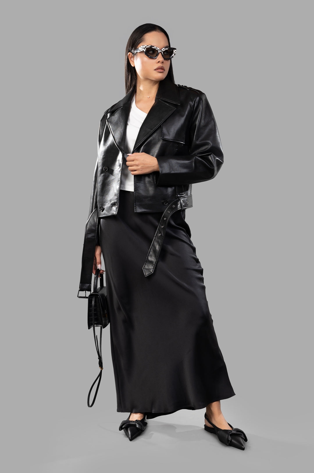 Anine Bing Greer Jacket in black leather, on-model view with wide shoulders and adjustable belt, styled with skirt and sunglasses.