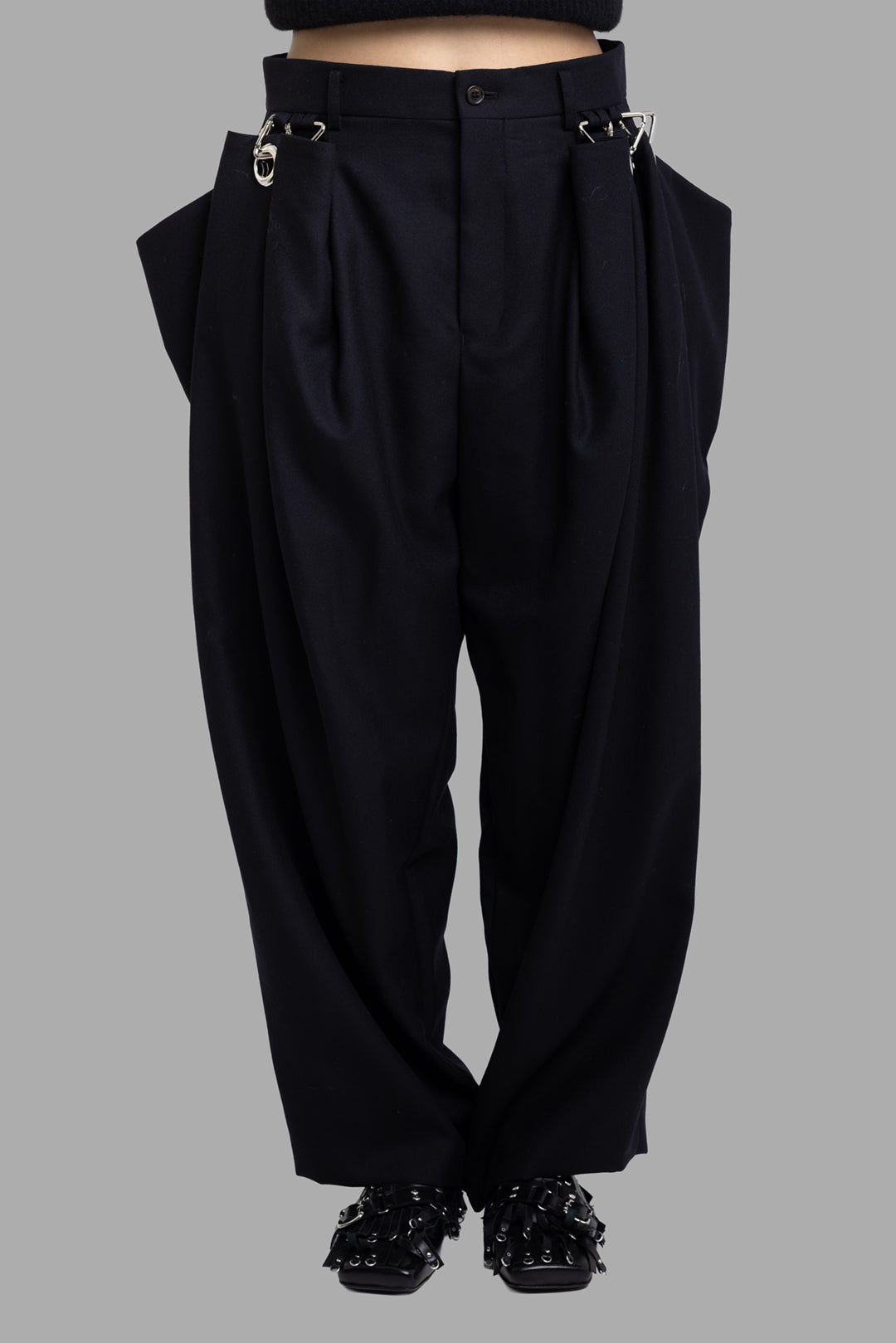 Noir Kei Ninomiya black wool trousers, close front view highlighting deep pleats and detachable side flap detail