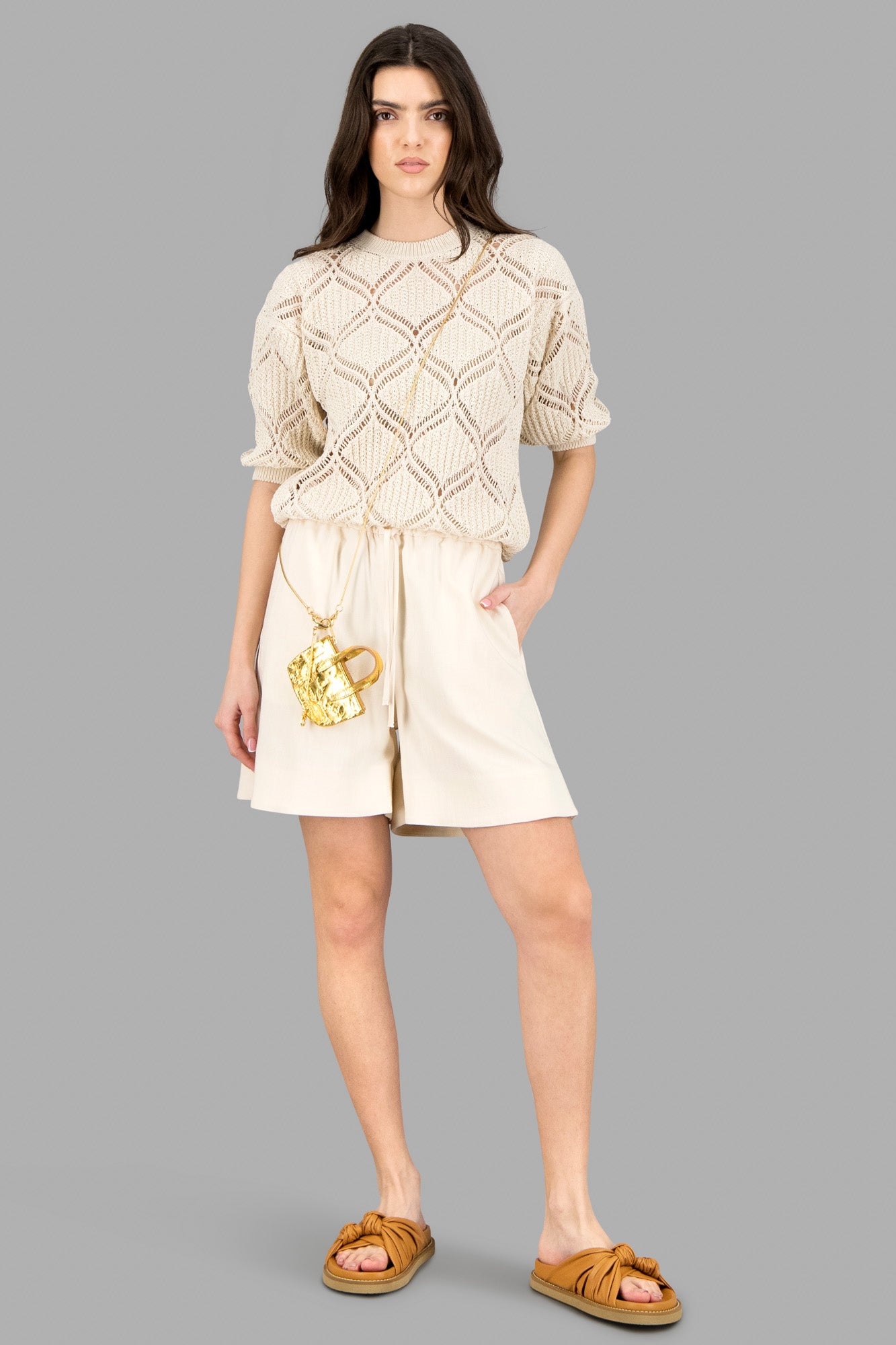 By Malene Birger Cream Shorts on-model with elastic waistband and drawstring ties, paired with a knit top and sandals.