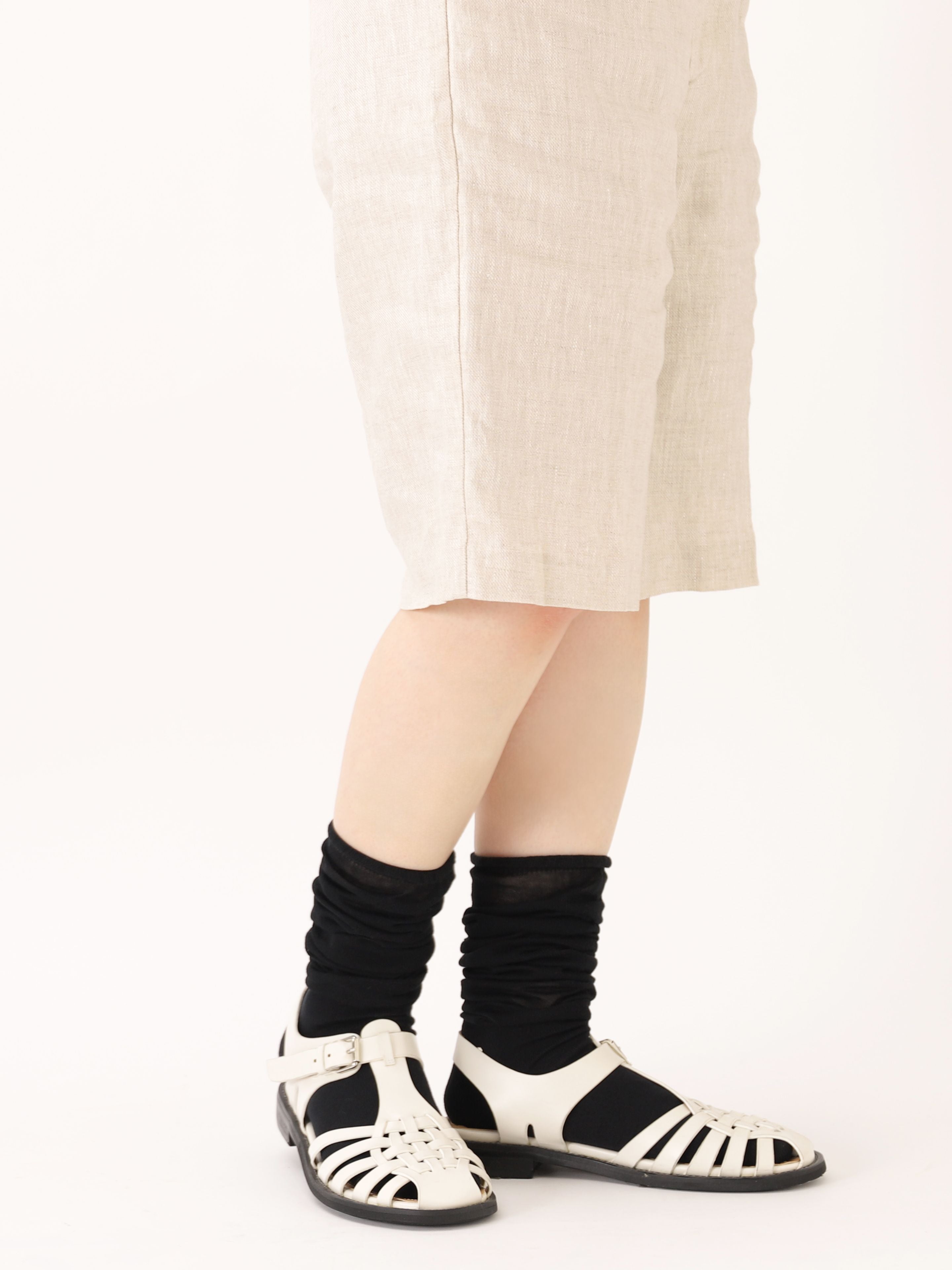 Tabio. Loose-style Light Knee High Socks worn slightly loose with white sandals, showcasing delicate black cotton fabric.