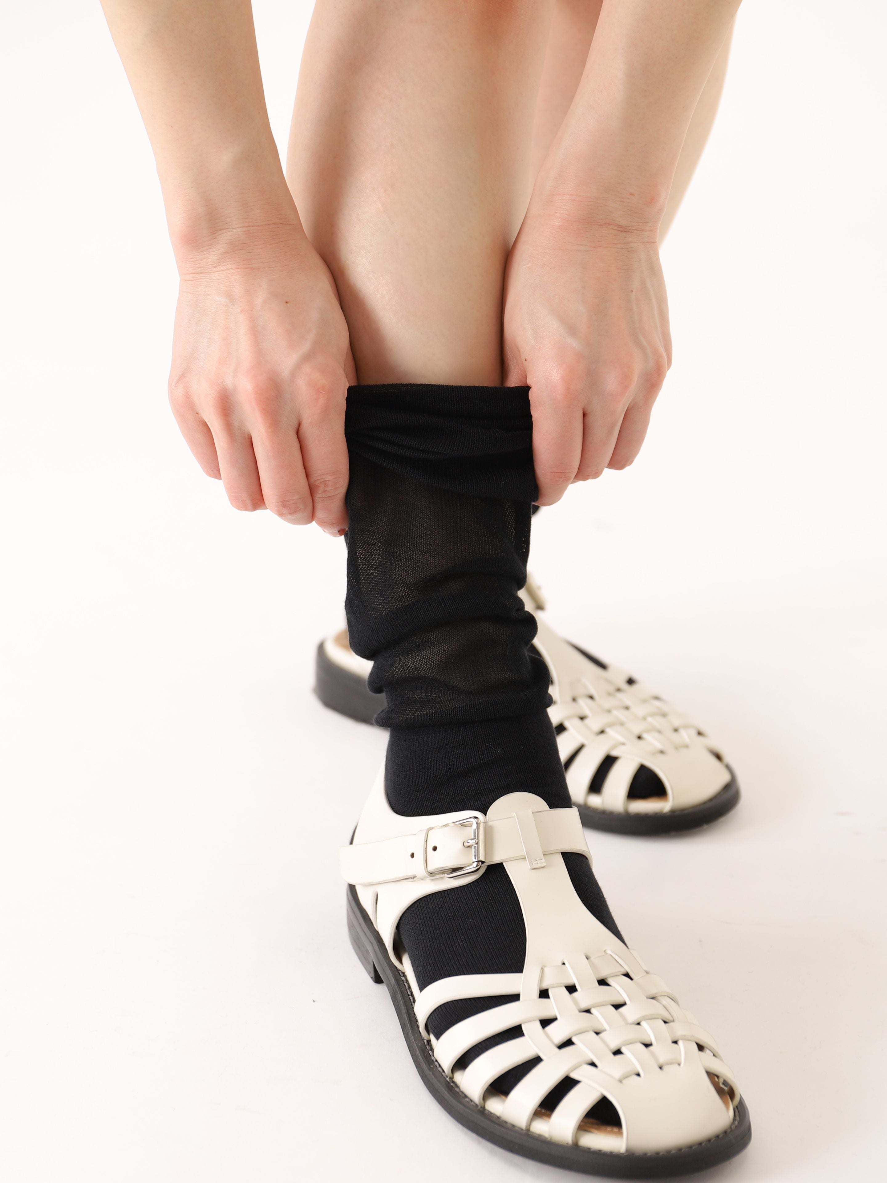 Tabio. Loose-style Light Knee High Socks shown being pulled up, featuring a delicate black transparent design, ideal for.