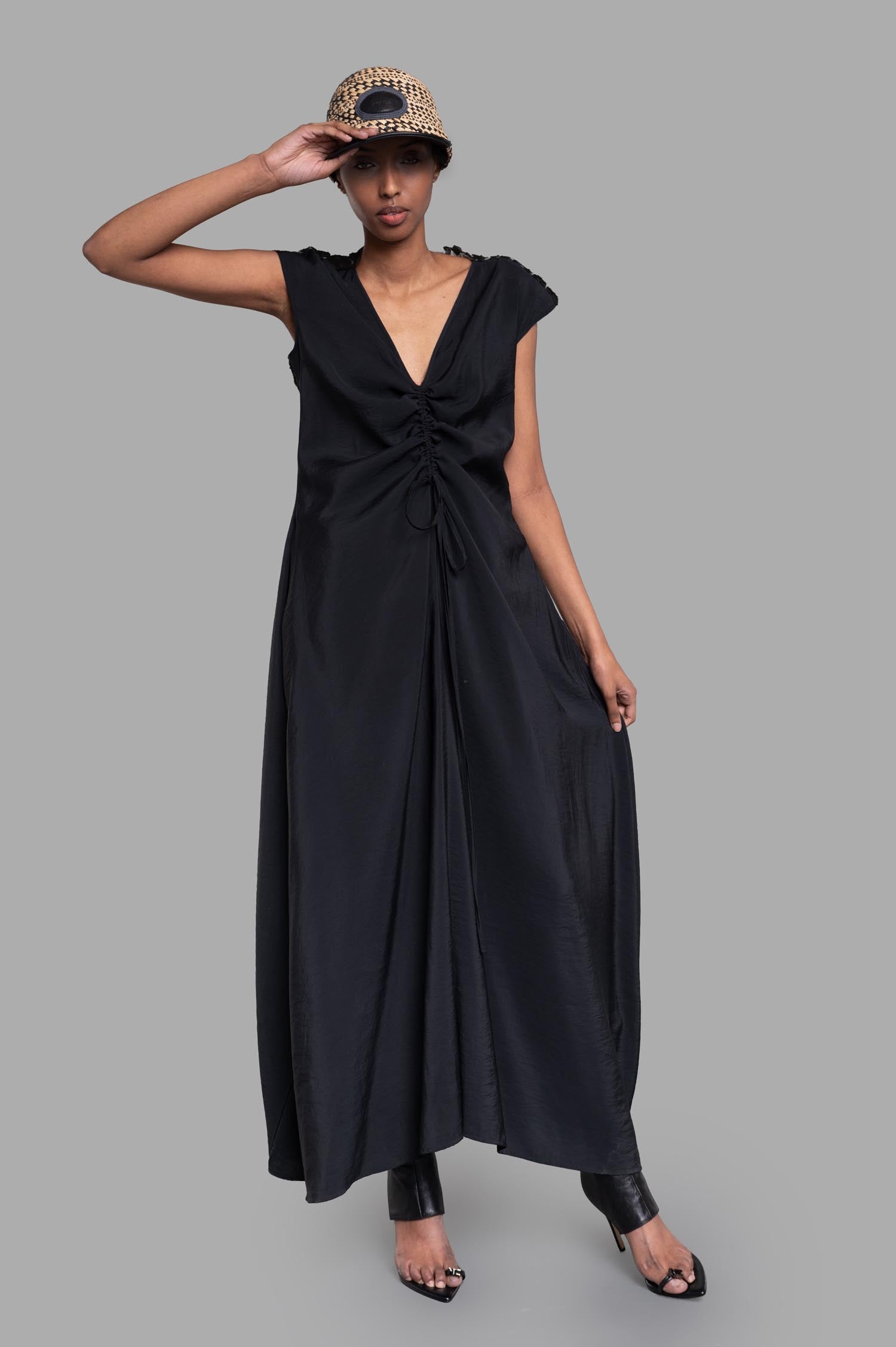 Gentry Portofino Gathered Dress in black with V-neck and cap sleeves, shown on a model wearing a hat, front view.