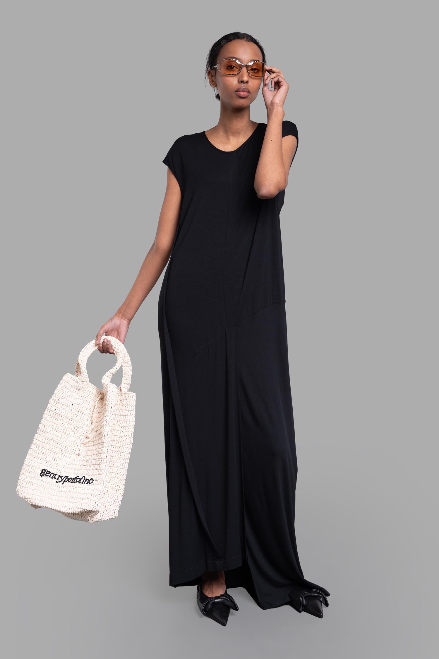 Gentry Portofino Paneled Column Dress in soft jersey, front view, cap sleeves, black, on-model with bag.