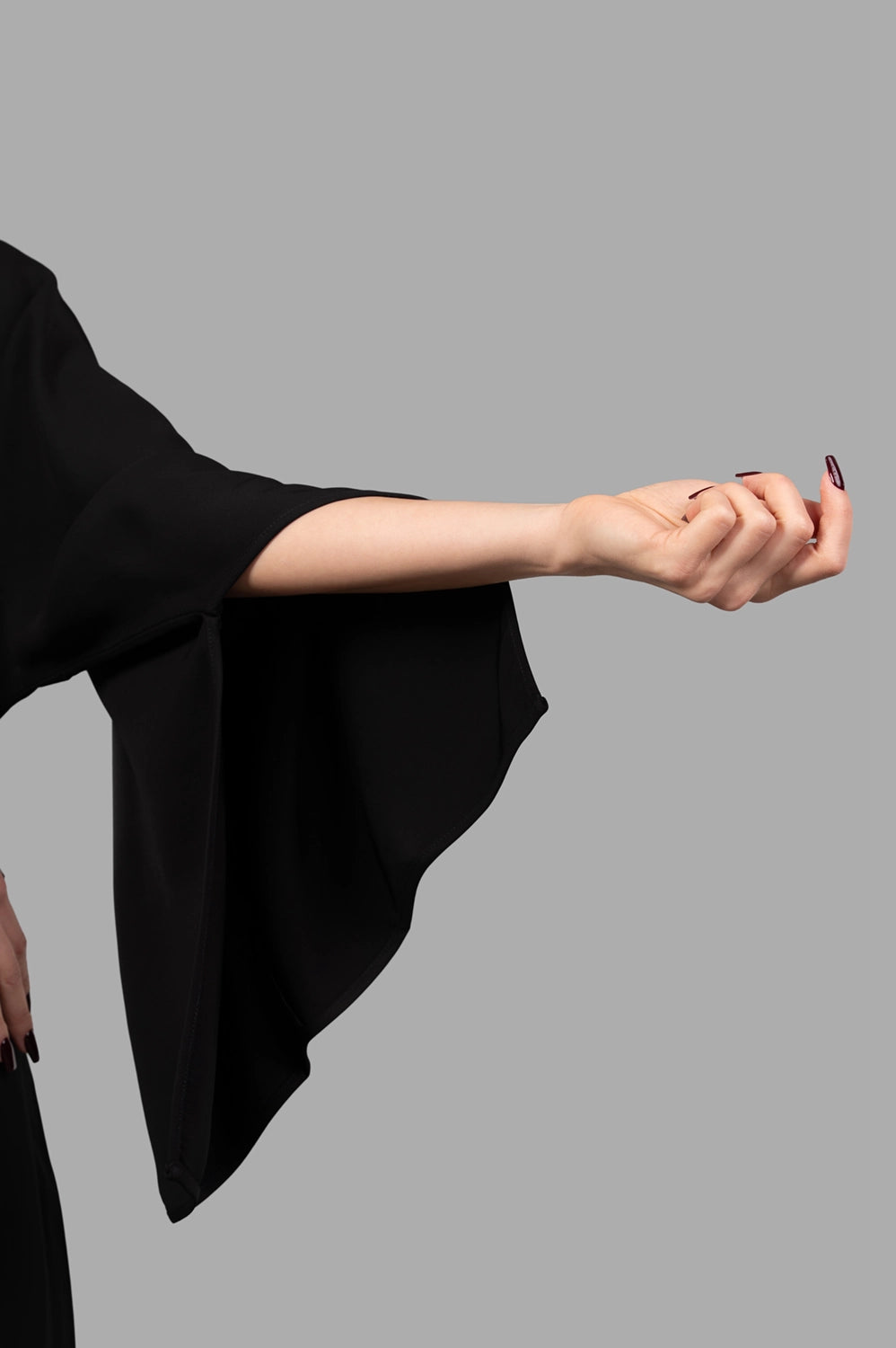 Person wearing a black dress with wide sleeves against a gray background