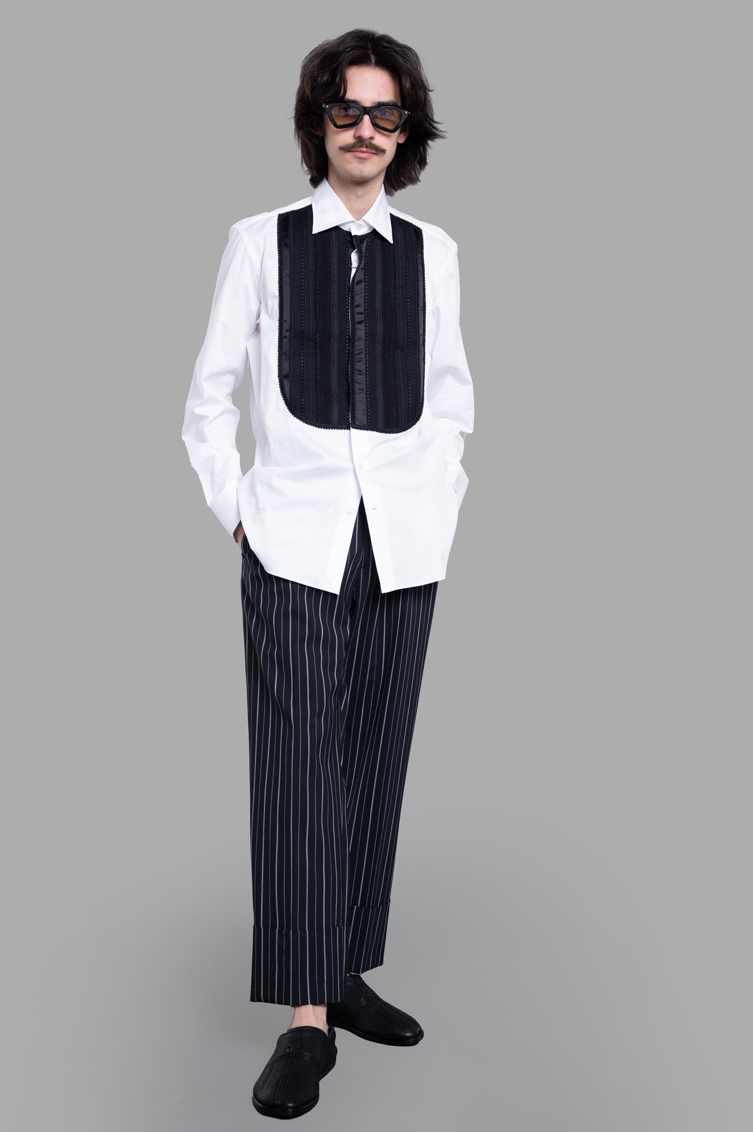 Junya Watanabe Bib Detailed Shirt, front view with model; stylish black bib on white shirt, paired with striped pants.