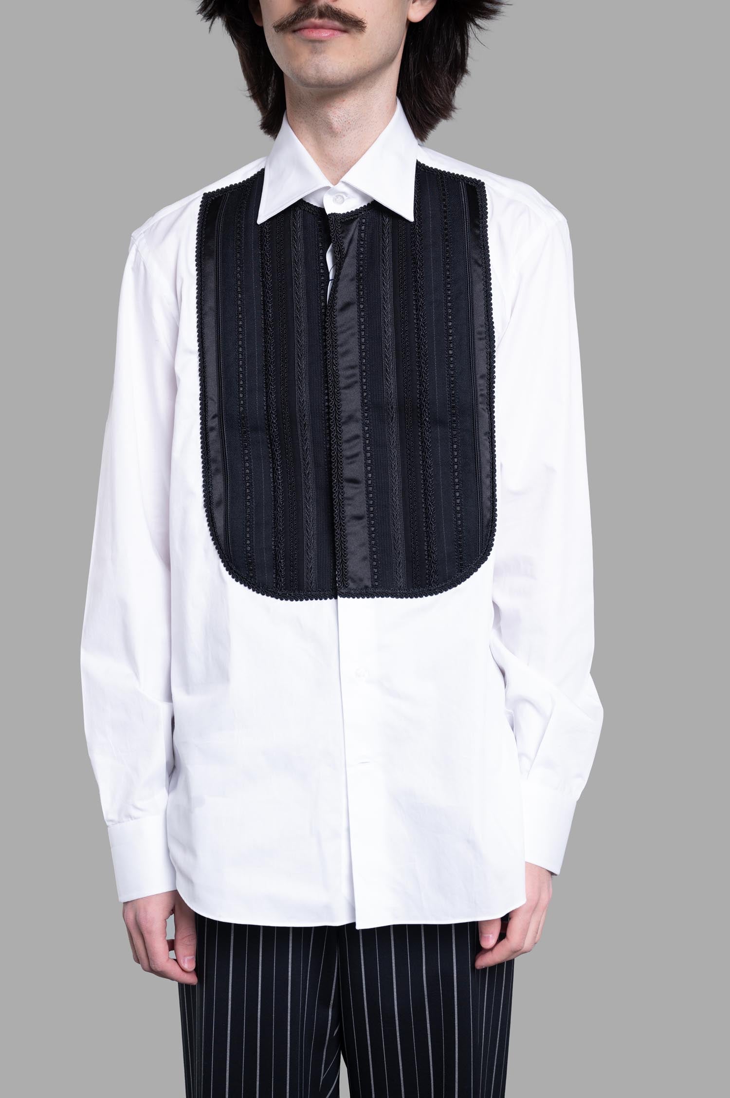 **Alt text:** Junya Watanabe Bib Detailed Shirt featuring a textured black bib on a model, styled with striped pants, front view.