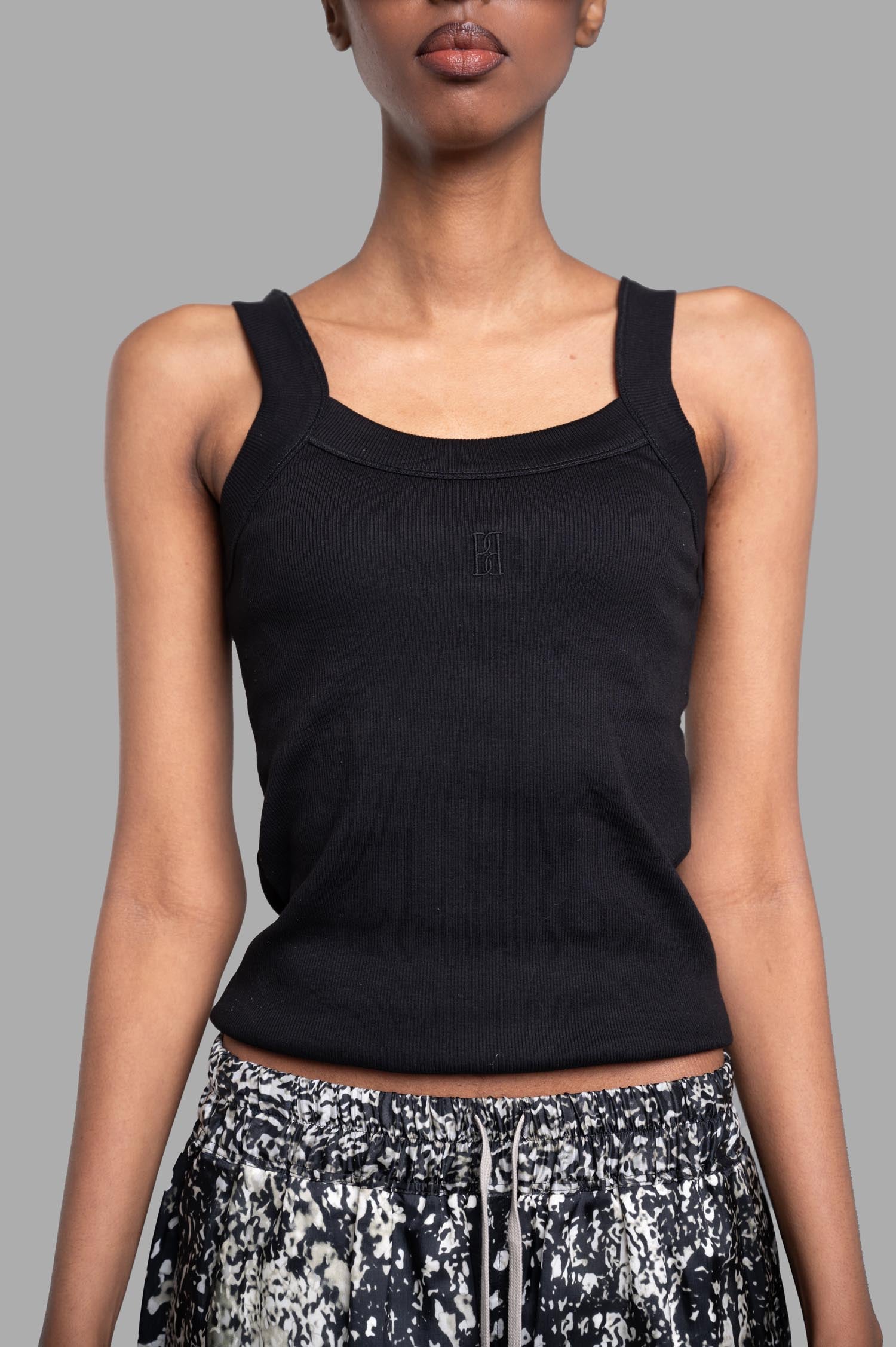By Malene Birger Frillio Top in black, featuring wide straps and embroidered monogram, styled on a model.