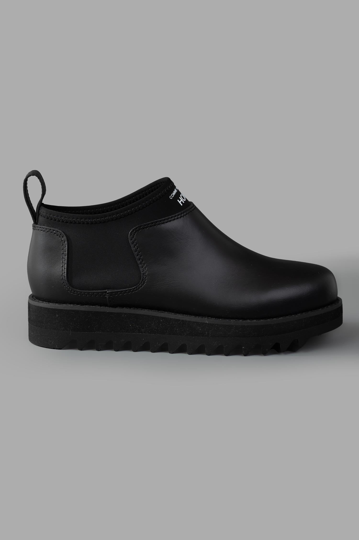 Comme des Garçons side view black Logo Leather Boots with rubber sole and pull tab, showcasing sleek design.