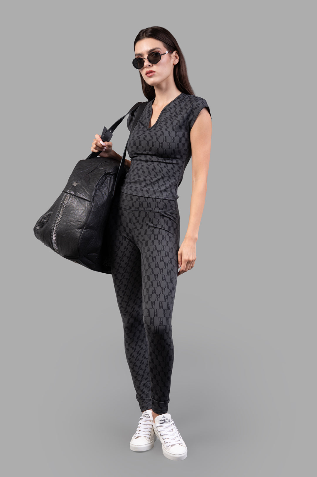 By Malene Birger Polene Athletic Leggings in black and grey, model wearing with matching top and sneakers, holding a bag.