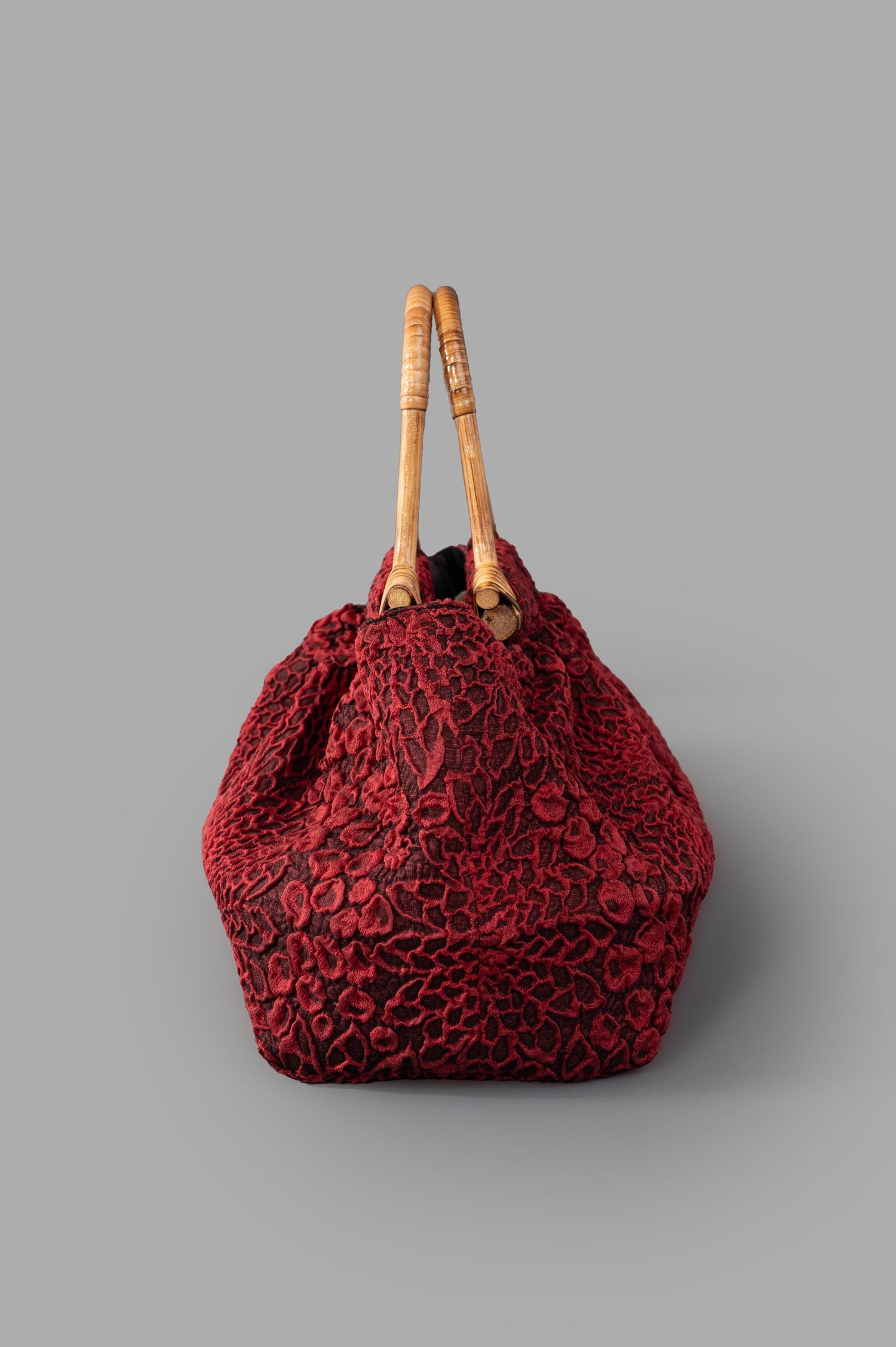 Marc Point Double-handle Bag featuring a textured floral design in red, showcasing the elegant structure and wooden handles.