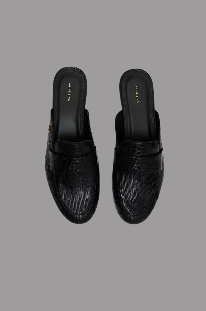 Anine Bing Corrine Mules in black leather with faux lizard texture, showcasing sleek slip-on design and embossed monogram detail.