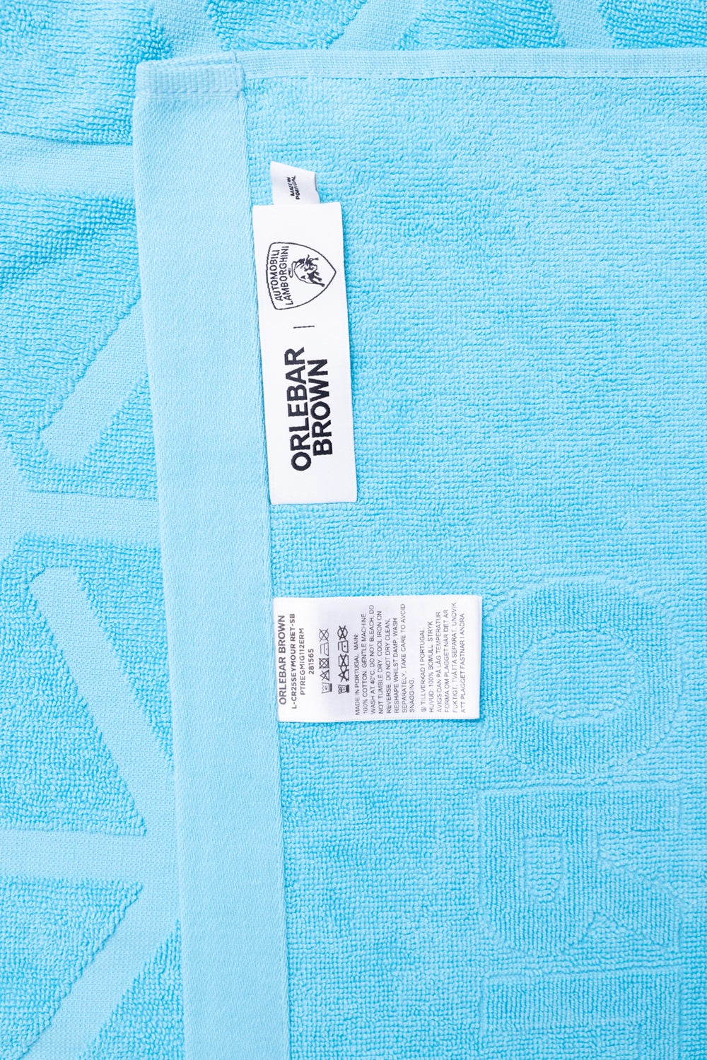 Orlebar Brown unisex beach towel in Synth Blue, care tag view, stitched brand label and wash symbols on terry cloth