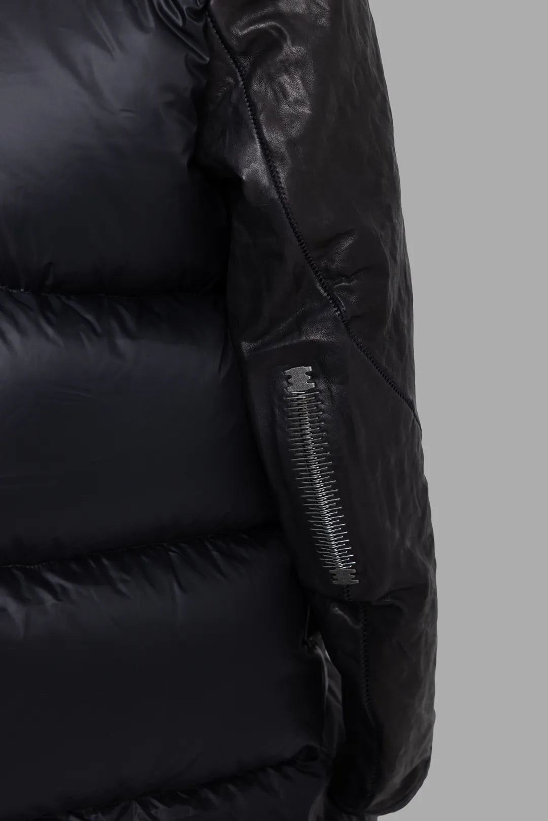 Isaac Sellam Experience unisex black coat, sleeve hardware close-up, leather arm panel with industrial staple zip detail.