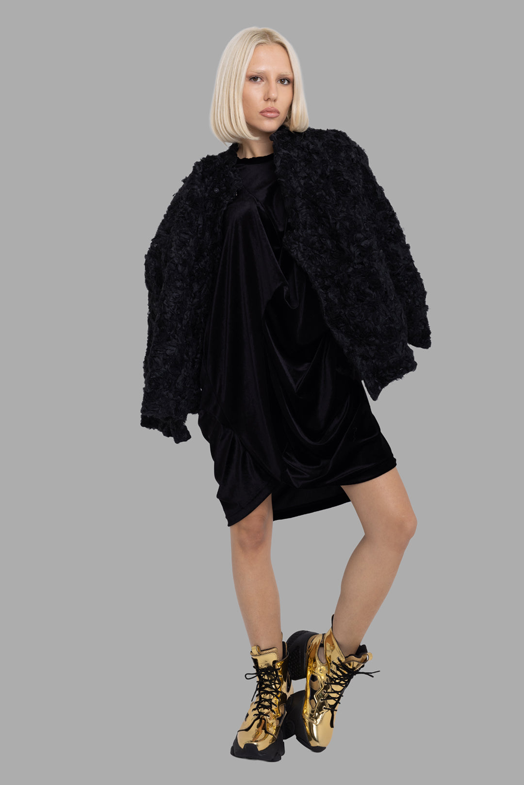 Comme des Garçons women's black draped dress, on-model full-length, layered under textured jacket with front drape folds.
