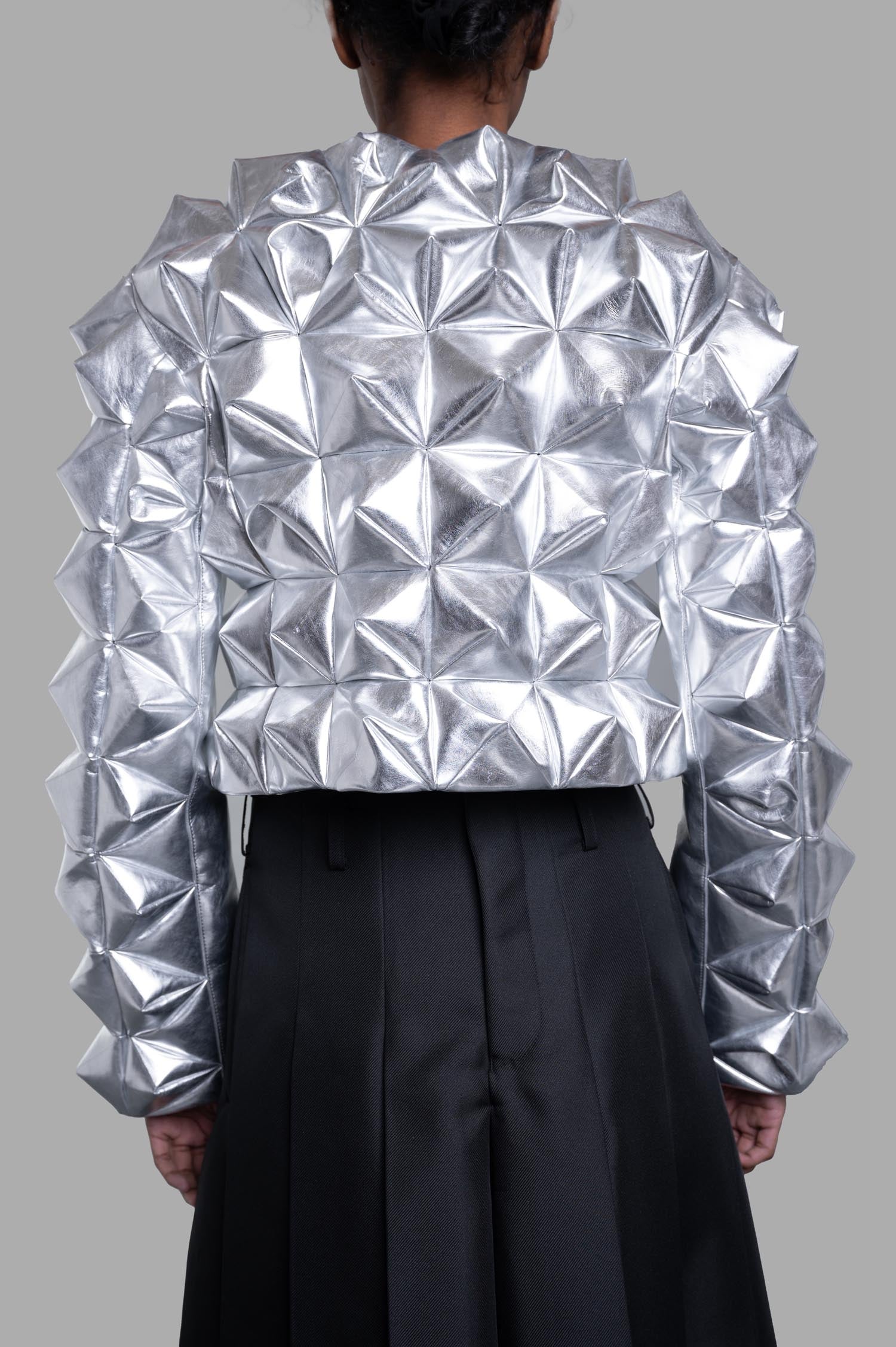 Junya Watanabe 3D-stud Jacket in Silver, back view on-model; metallic pyramid-textured sleeves and body over black skirt.