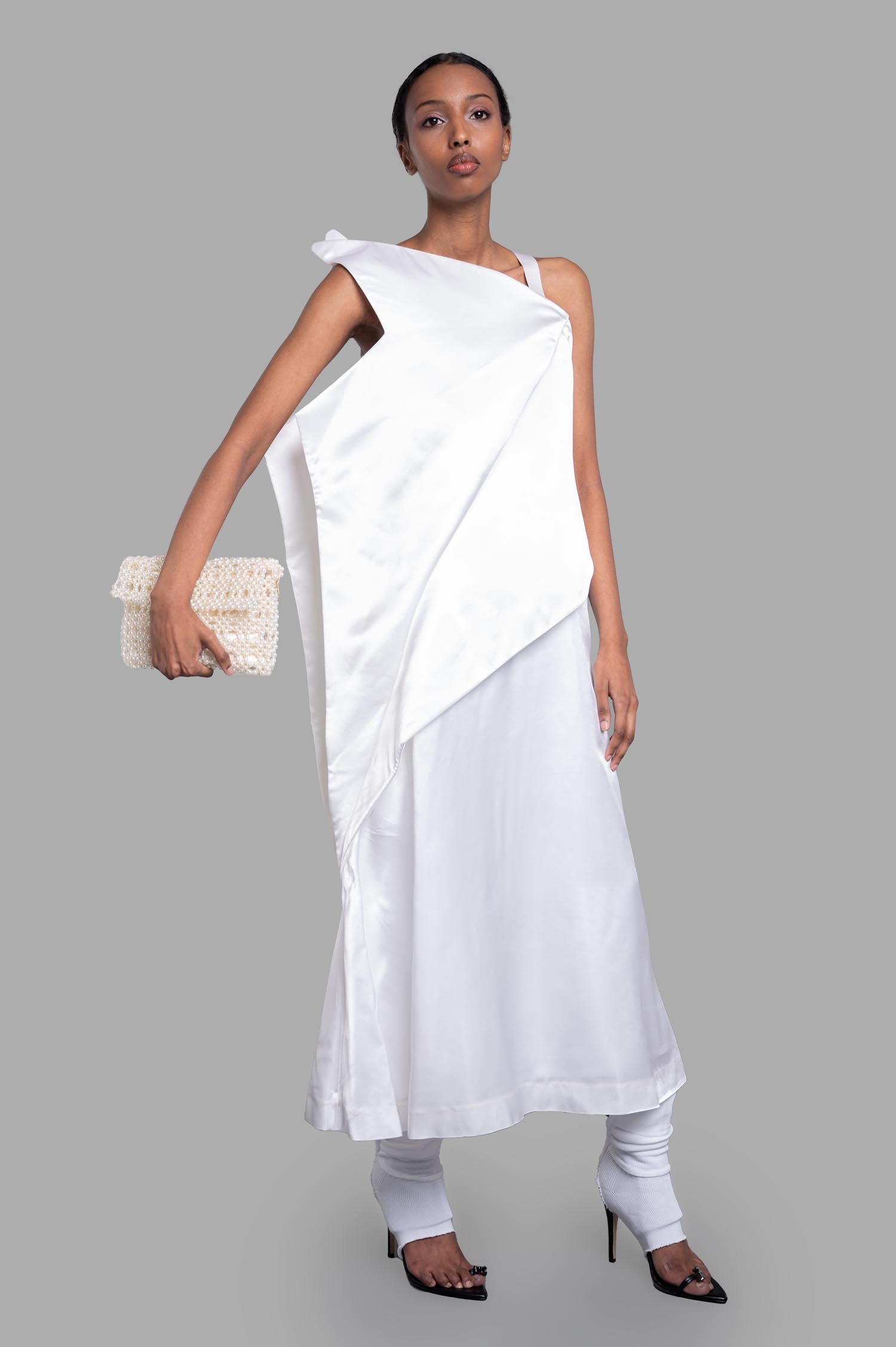 Noir Kei Ninomiya Asymmetric Dress in White, front view on-model, elegant draping, unique design, paired with clutch.