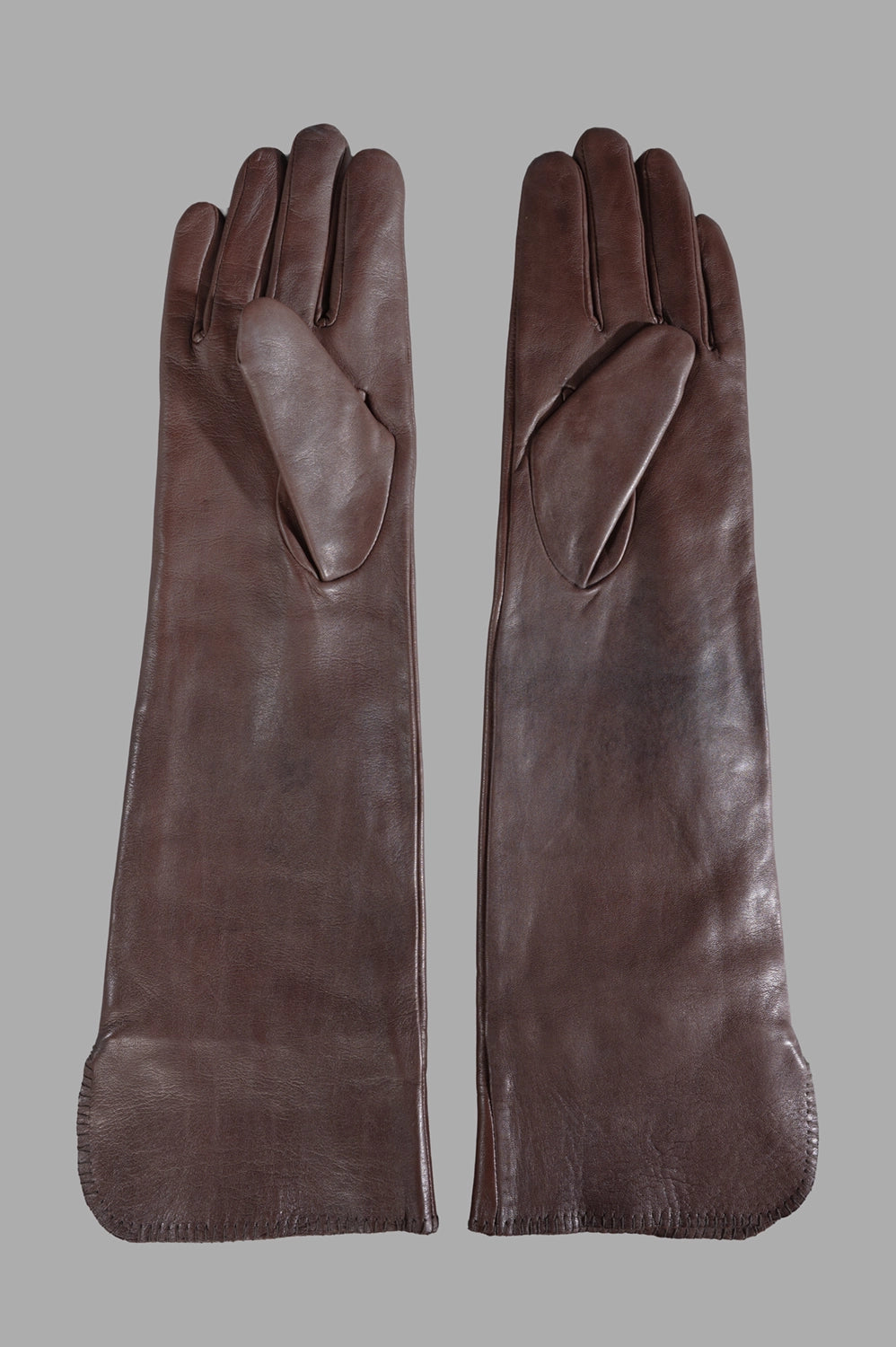 Front close-up of long brown leather gloves showing elongated cuffs and stitched monogram