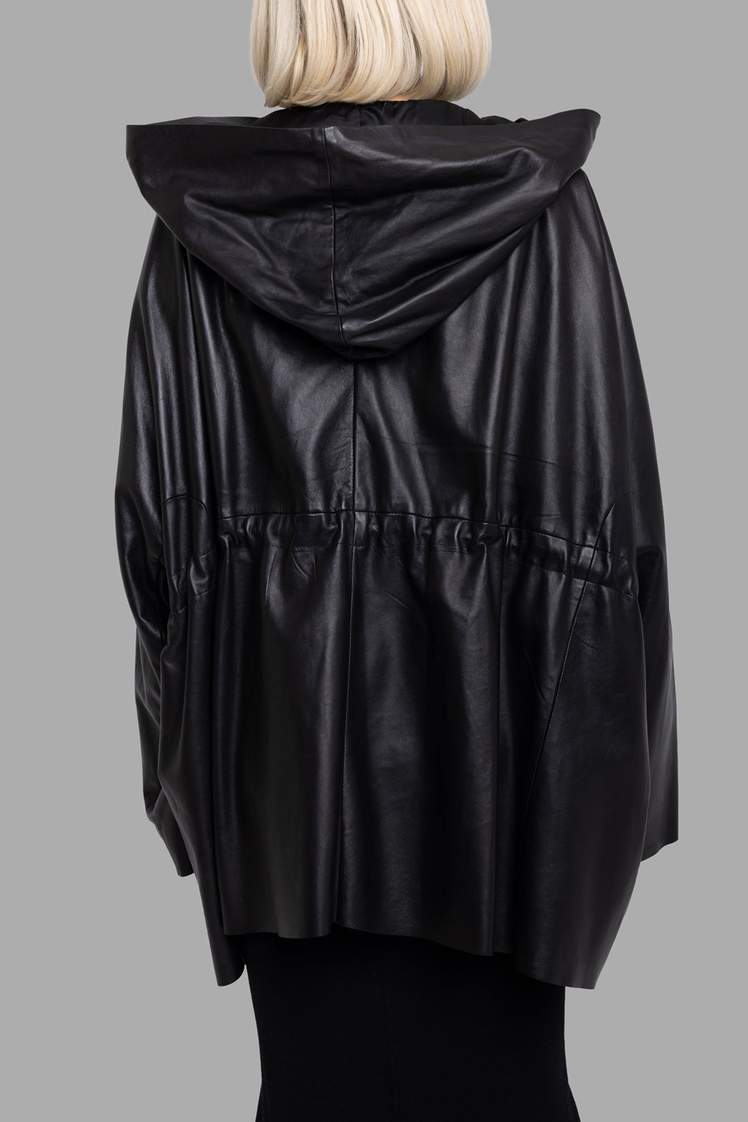 Rick Owens women's black hooded leather jacket, back view showing gathered waist seam and fluid oversized drape.