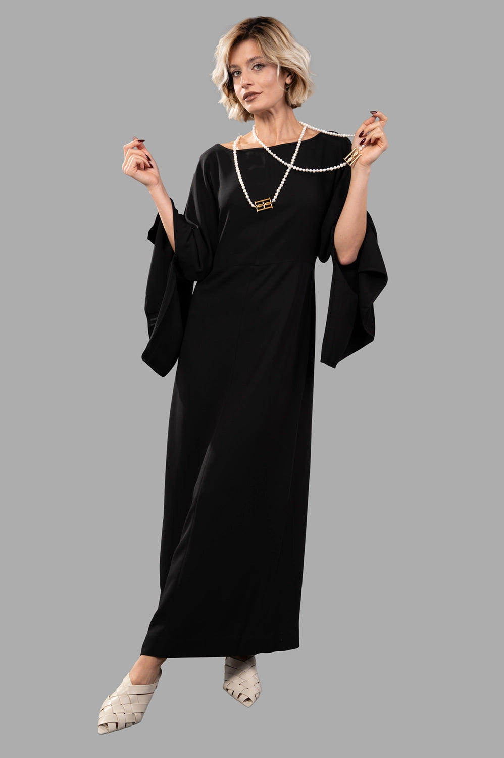 Full-length view of black maxi dress on model, relaxed fit with draped sleeves and bateau neckline