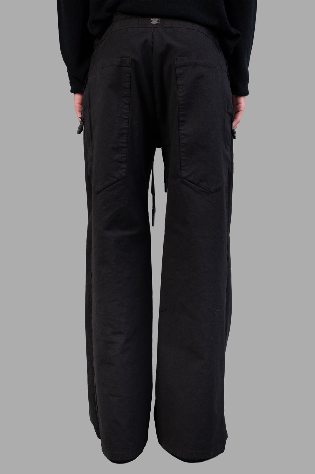 Isaac Sellam Drawstring Trousers in black, showcasing wide-legged silhouette and relaxed drawstring waist from the back view.