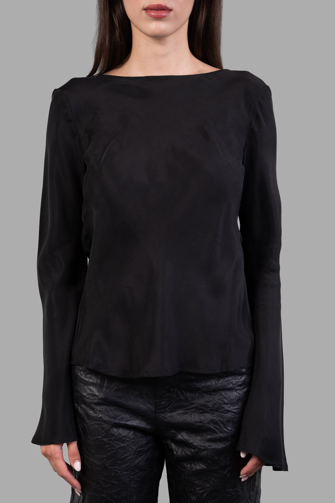 By Malene Birger. Laura Blouse in black, featuring a smooth drape and long sleeves, styled on model with fitted pants.