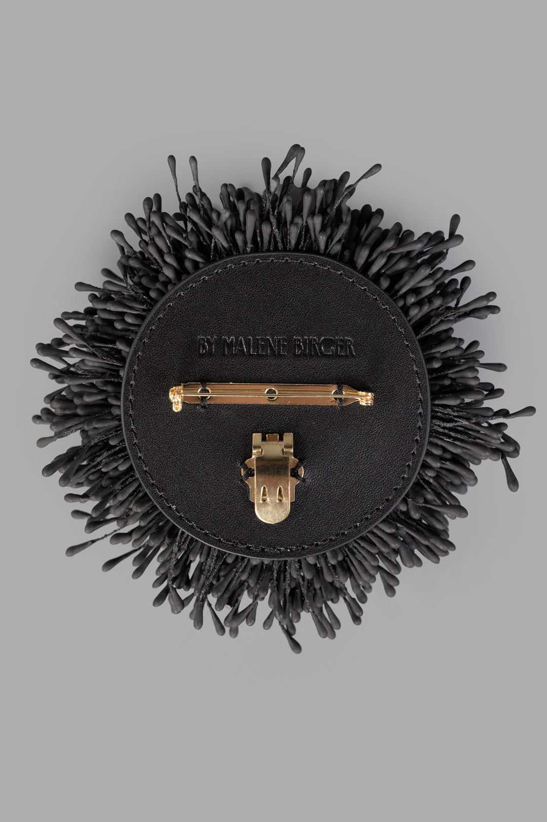 By Malene Birger Henna Brooch in Black, featuring a textured, organic design with gold-tone fastener, viewed from above.