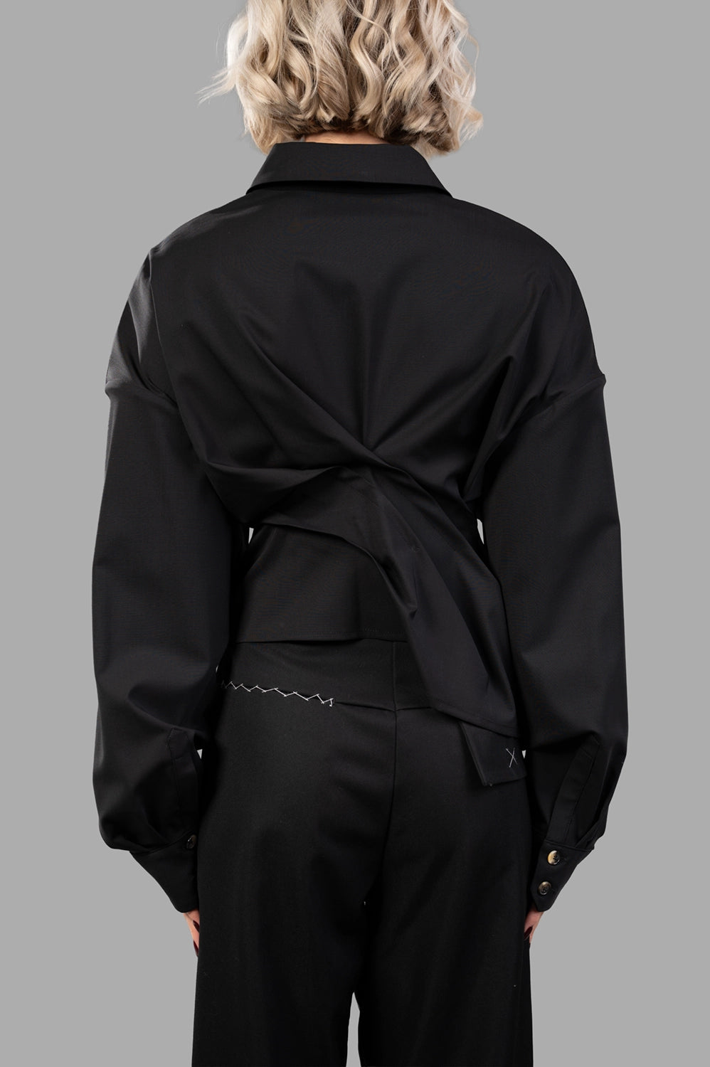 Back close-up of black twisted shirt showing wrapped panels and buttoned cuffs