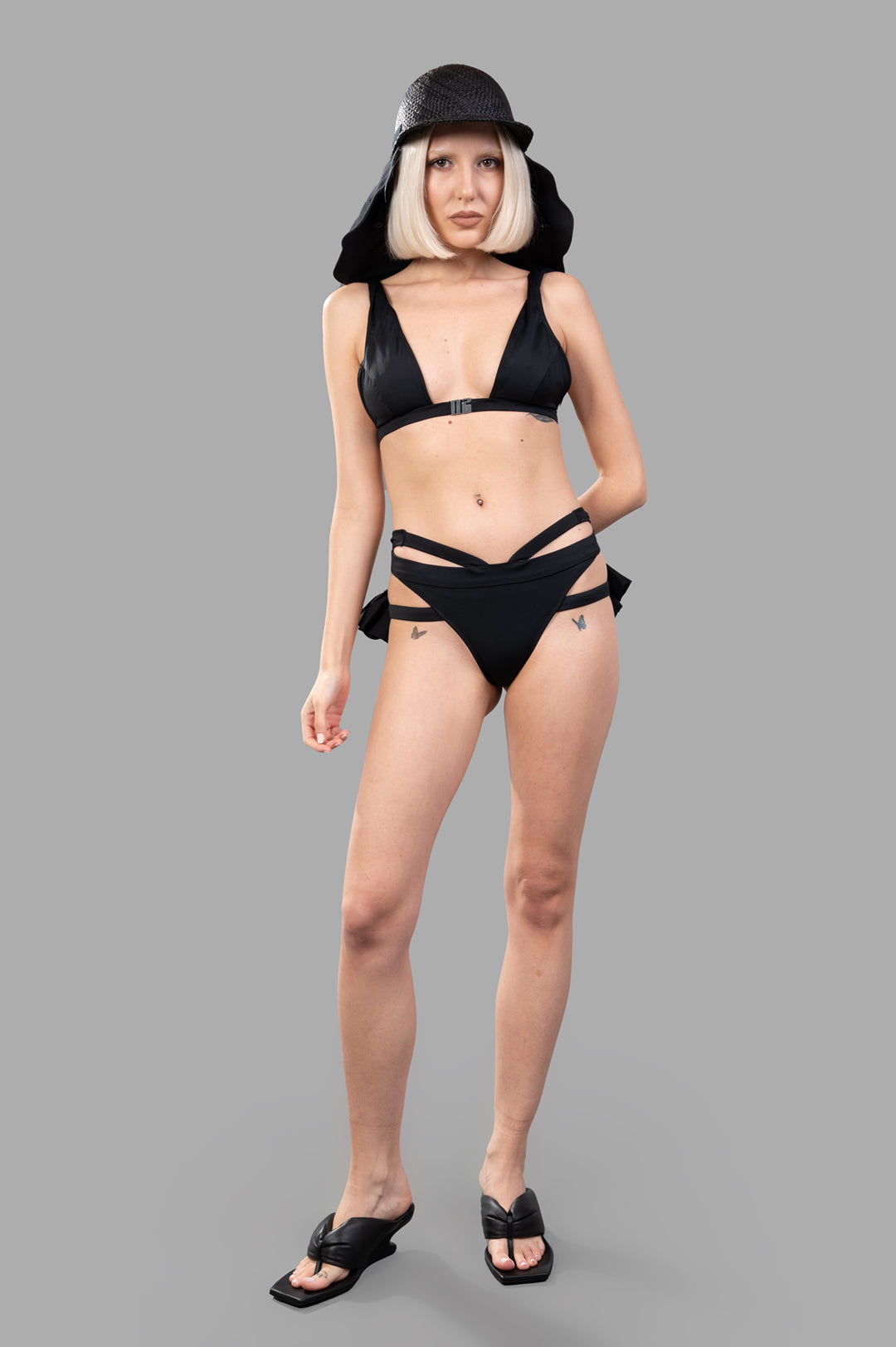 Natasha Zinko Ruffled Bikini Set in black, front view on-model, featuring triangle top and multi-strap bottoms with ruffles.