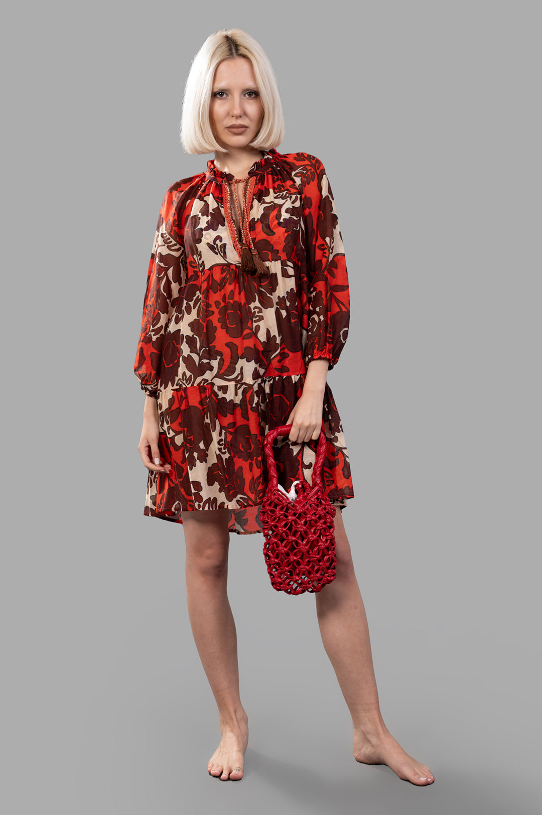 Anjuna Naike Mini Dress in red on model, front view. Features a floral pattern, ruffled details, and a front tie closure.