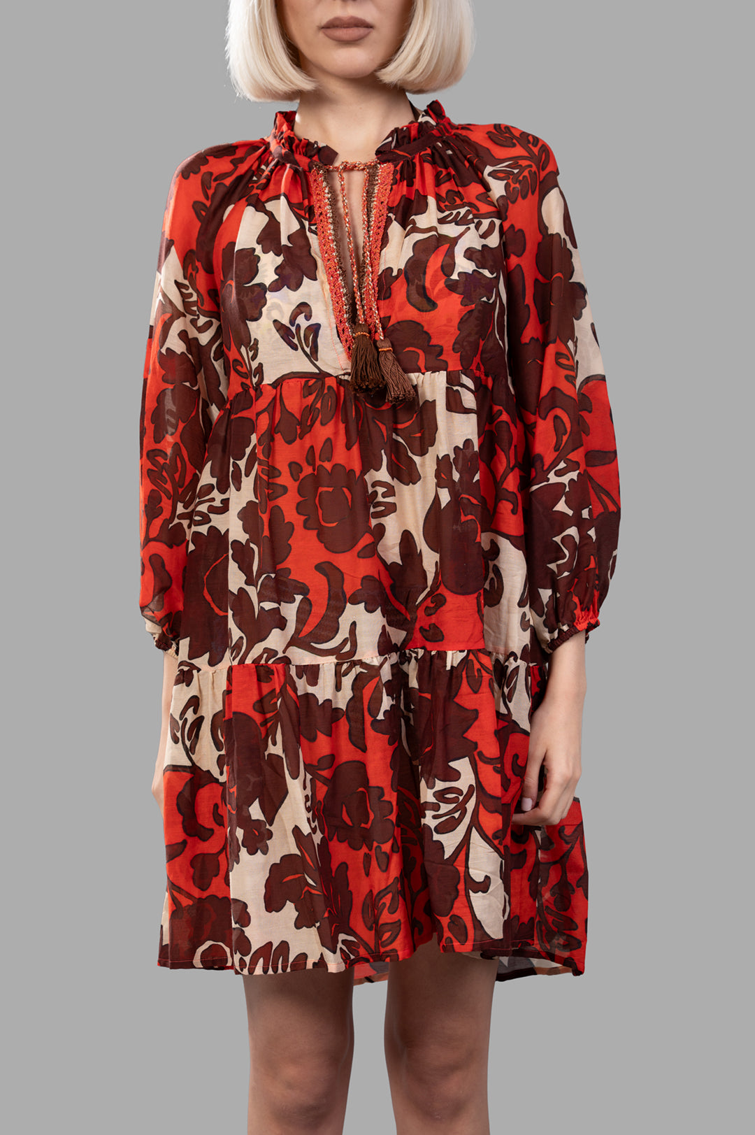 Anjuna Naike Mini Dress in a vibrant brick red with a front tie, ruffled details, and elasticated cuffs, shown on model.