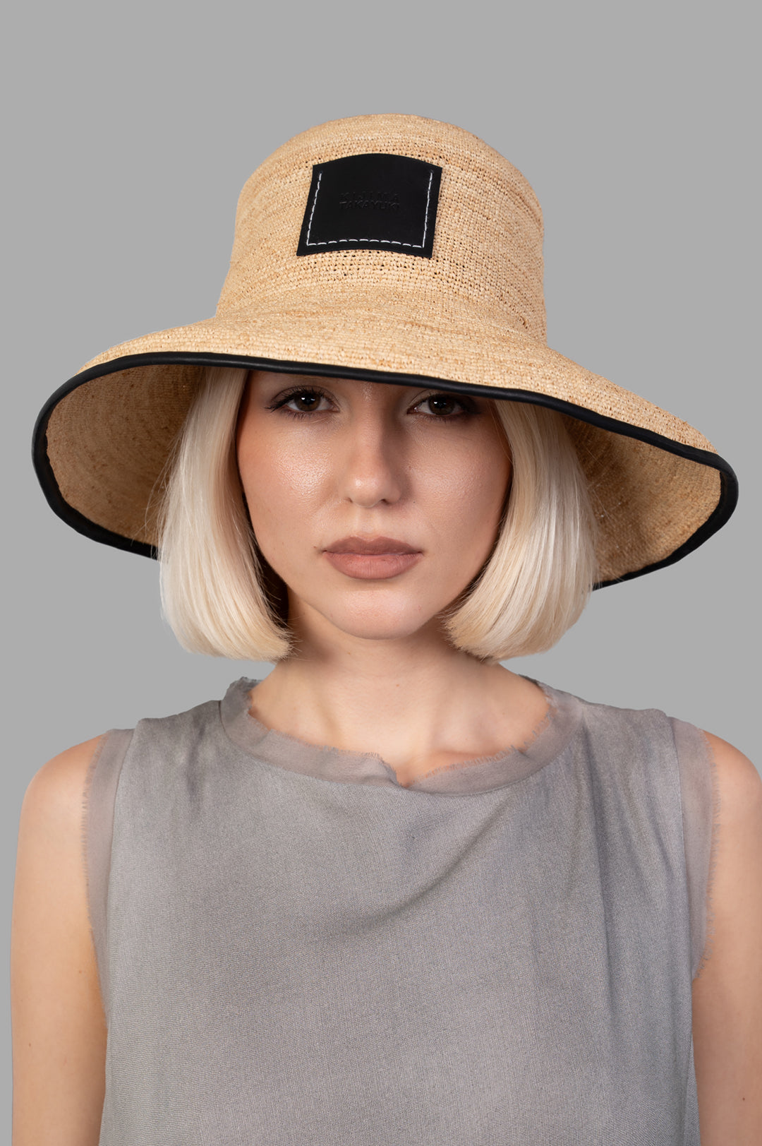 Kijima Takayuki Straw Mushroom Hat in natural raffia, worn by model, featuring a contrasting black trim and logo patch.
