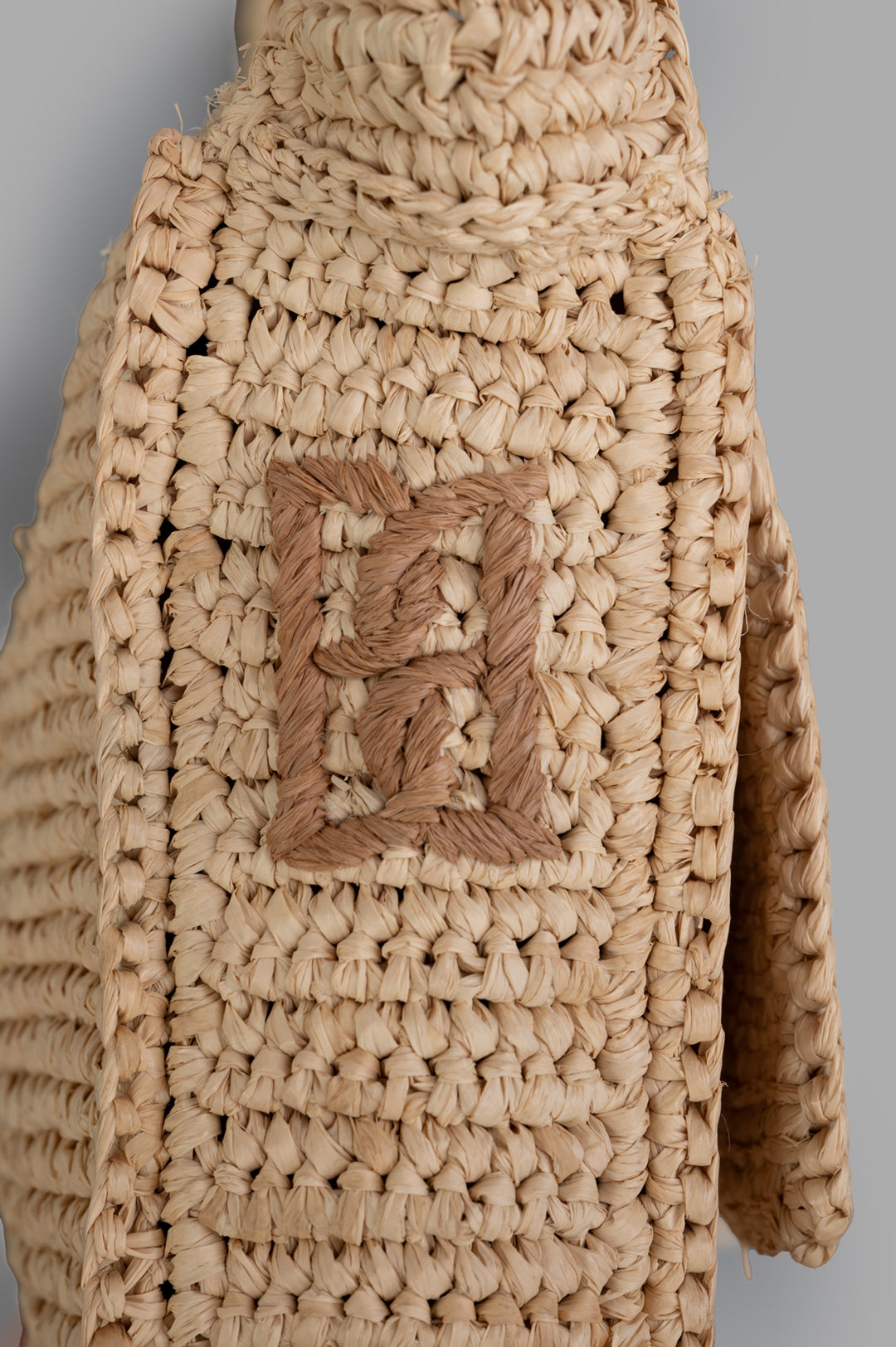 By Malene Birger Miro Shoulder Bag close-up of the embroidered monogram on natural raffia, showcasing its artisanal texture.