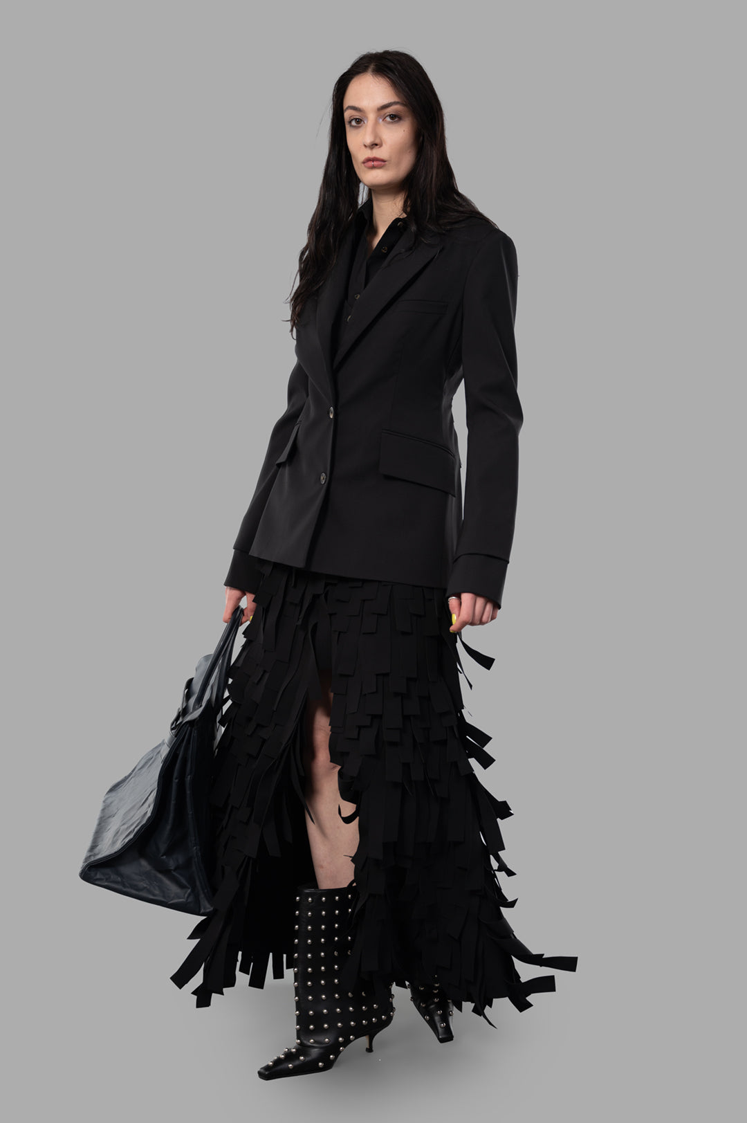 A.W.A.K.E. MODE Open-Back Blazer, front view on-model, black wool blend, paired with fringed skirt and studded boots.