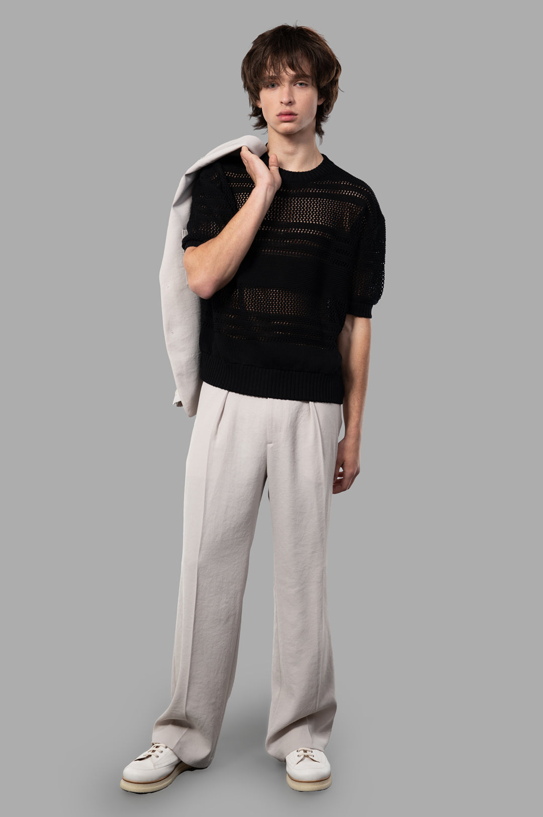 Vein Pleated Trousers in beige, relaxed fit with front pleats, shown on model holding jacket over shoulder.