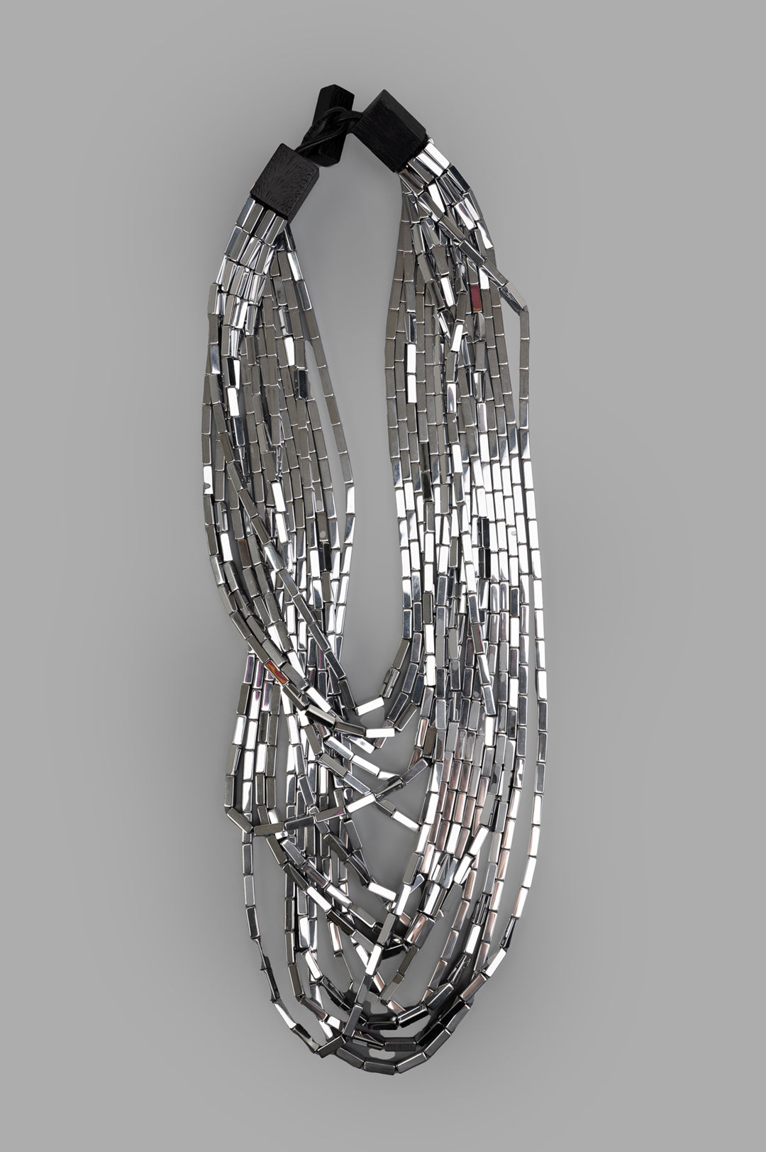 Monies Silva Necklace front view, featuring layered silver hematite beads with a bold, artistic design on a grey background.