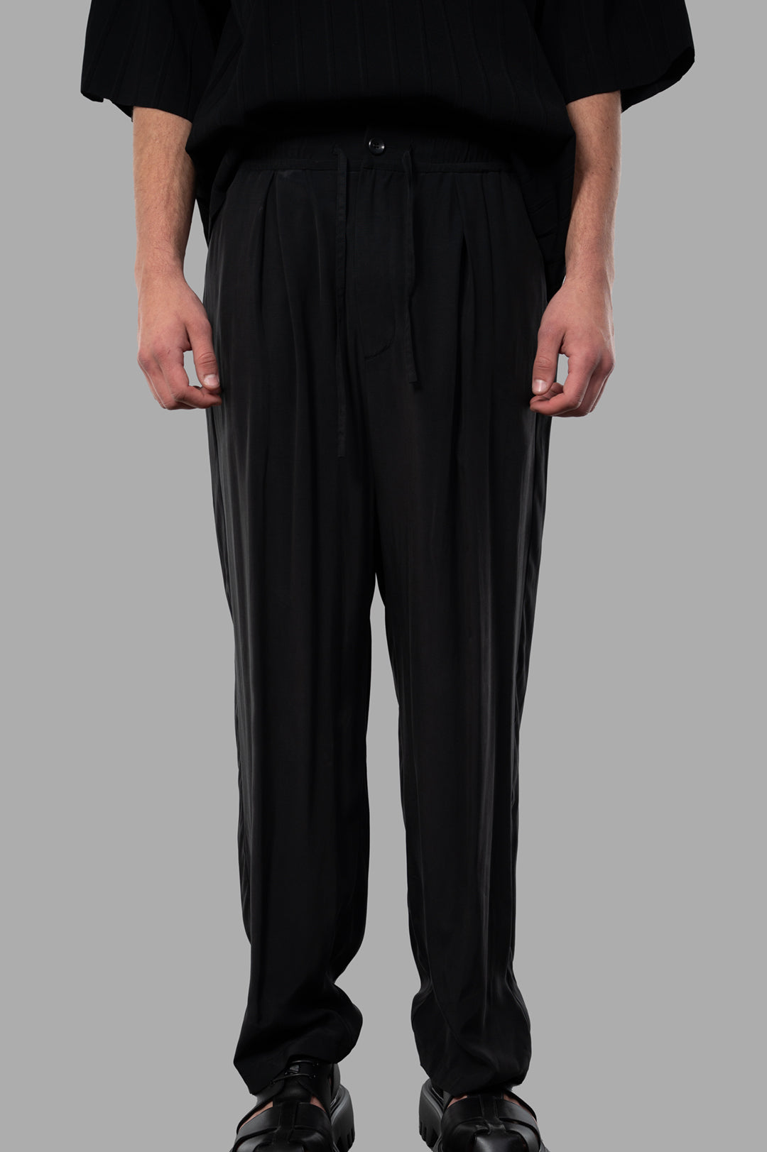 Attachment Pleated Trousers in black with relaxed fit, side pockets, and elastic drawstring waistband, shown on model.
