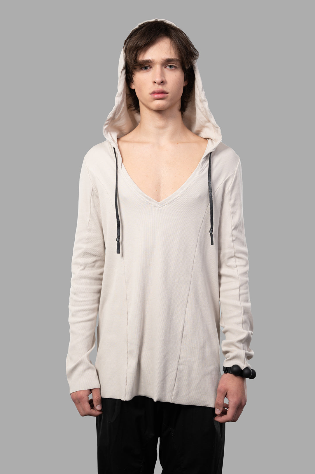 Justin Gall Light Rib Hooded Top featuring a model in a beige ribbed V-neck hoodie with raw cut sleeves and waxed cotton.